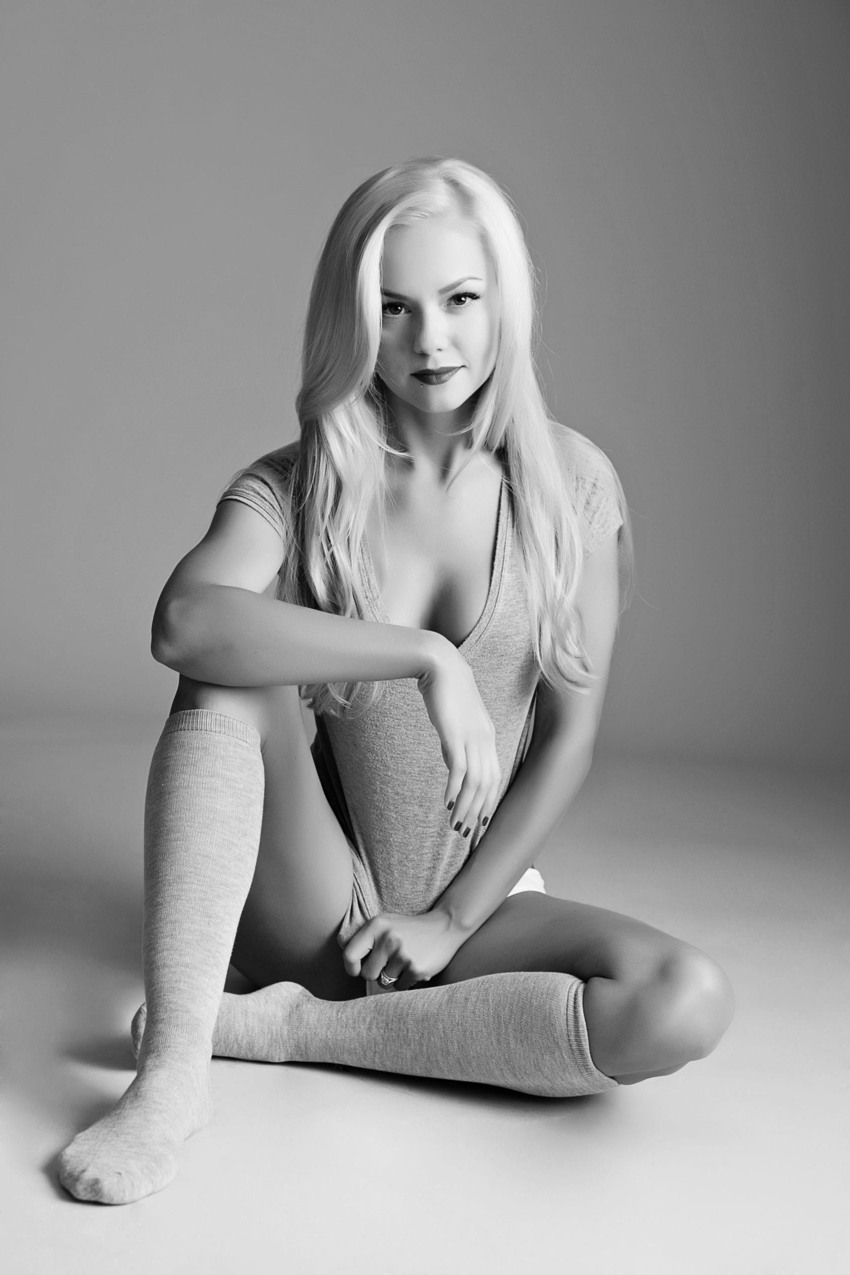 Blonde woman in a knitted sweater and socks, sitting and looking at the camera, black and white.