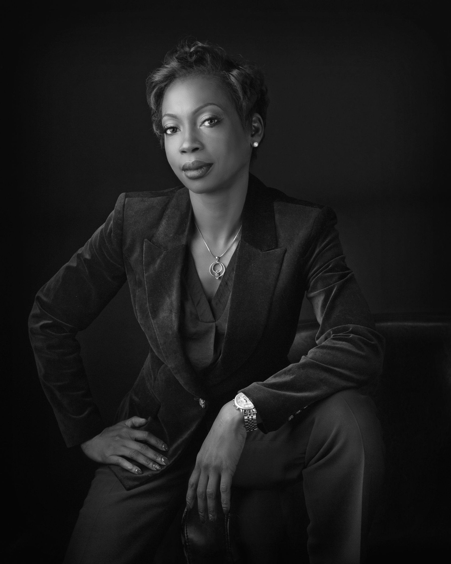 Woman in a suit poses with hand on hip. Dark setting, black and white photo.