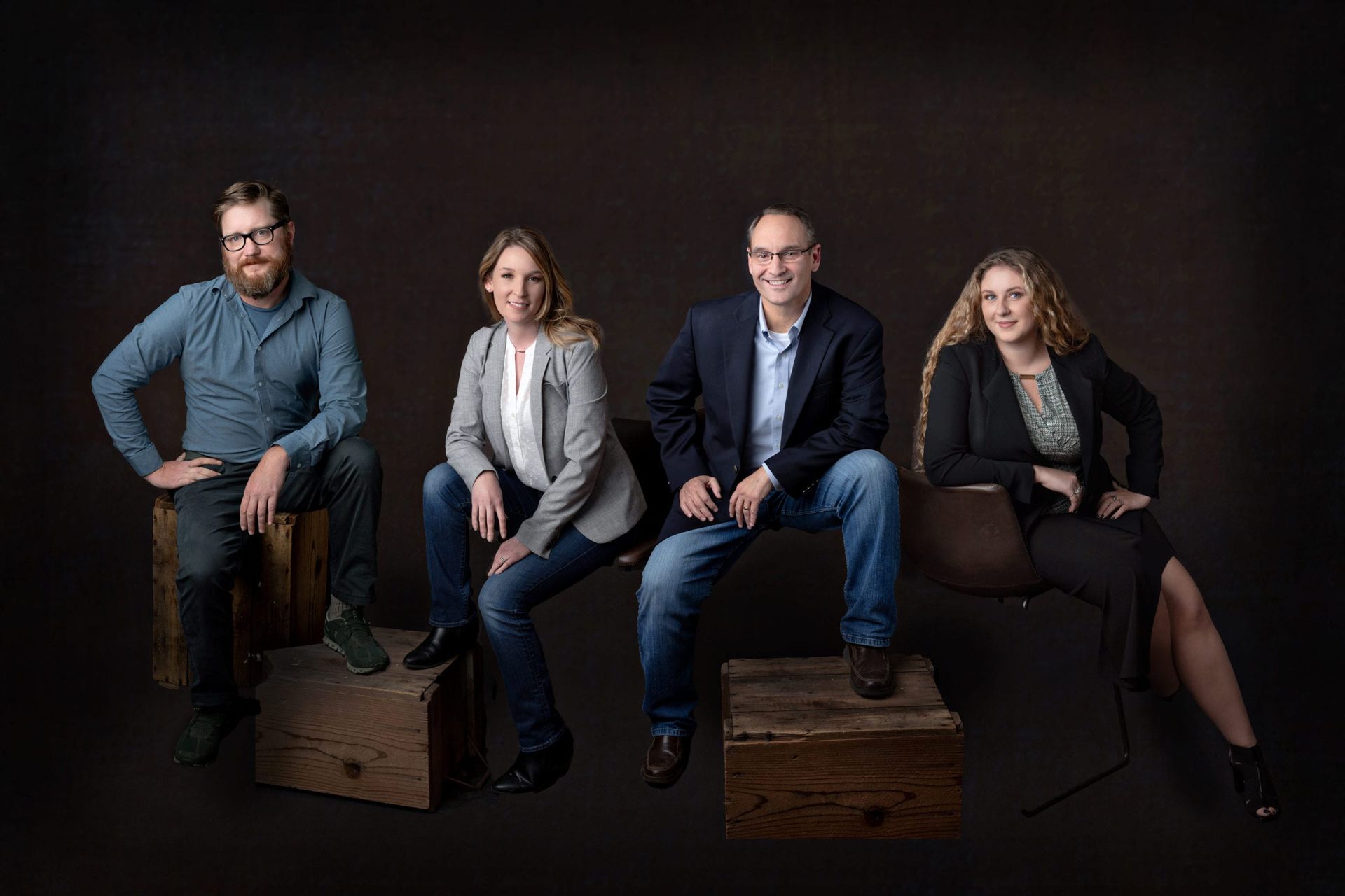 Group of four people seated, smiling, on wooden blocks against a dark background.