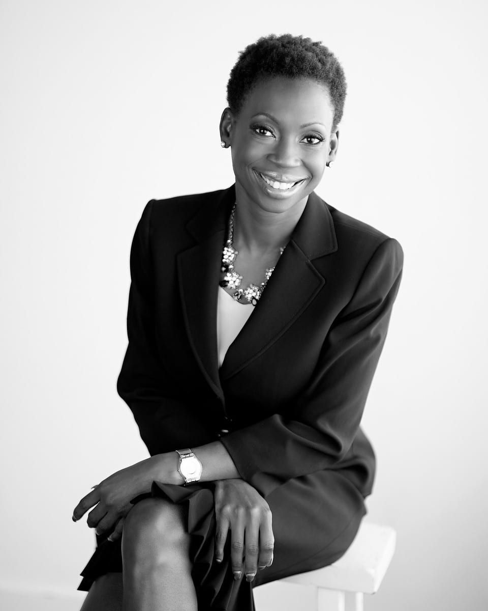 Black and white portrait of a smiling woman in a suit, sitting, looking at the camera.