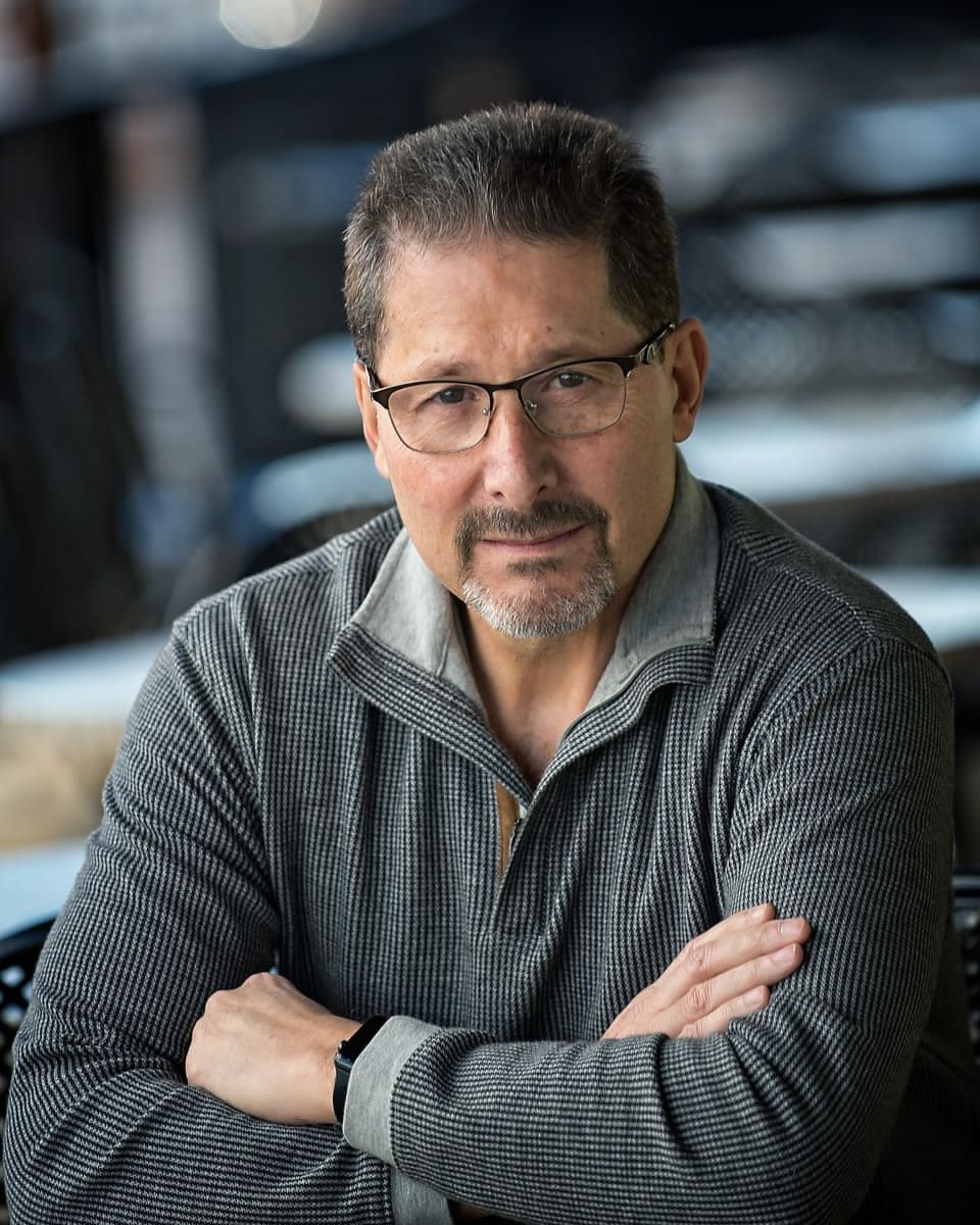Man with glasses, arms crossed, gray textured sweater, looking at camera.