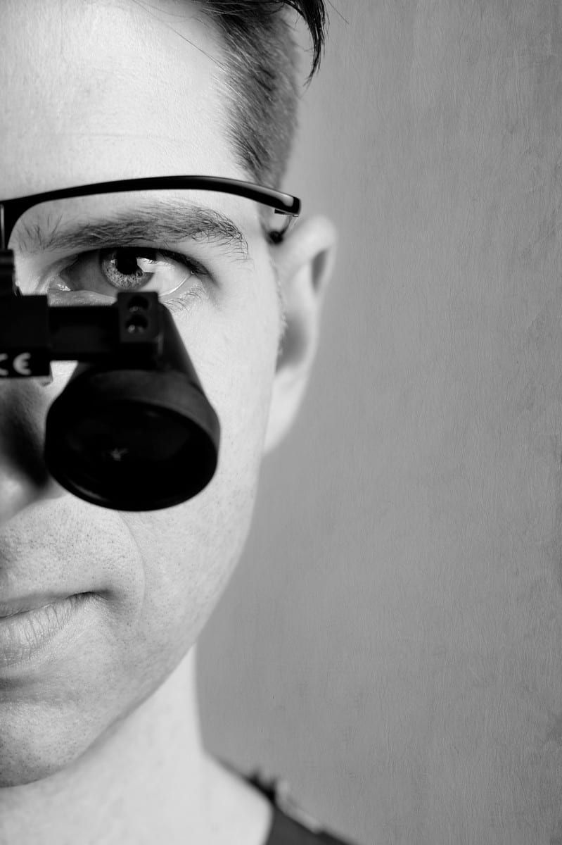 Man with magnifying glasses over one eye, in black and white.