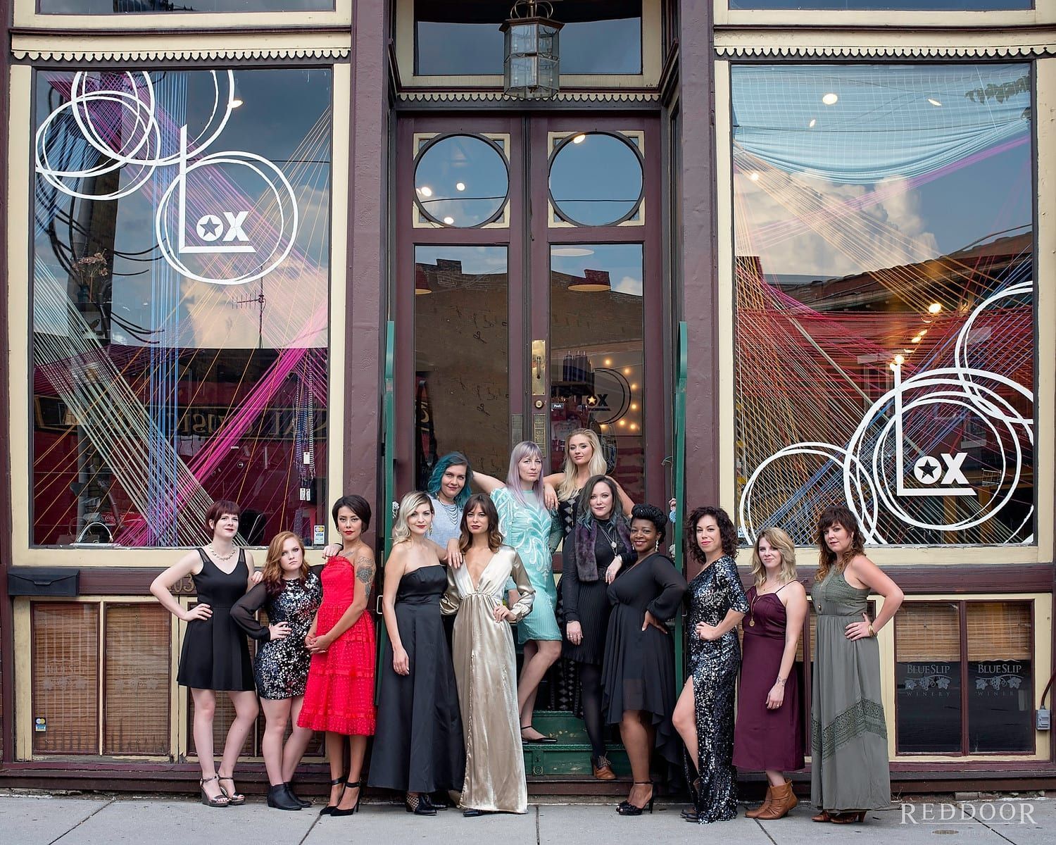 Group of women outside a salon called Lox, posing and smiling. Building has large windows with decorative art.