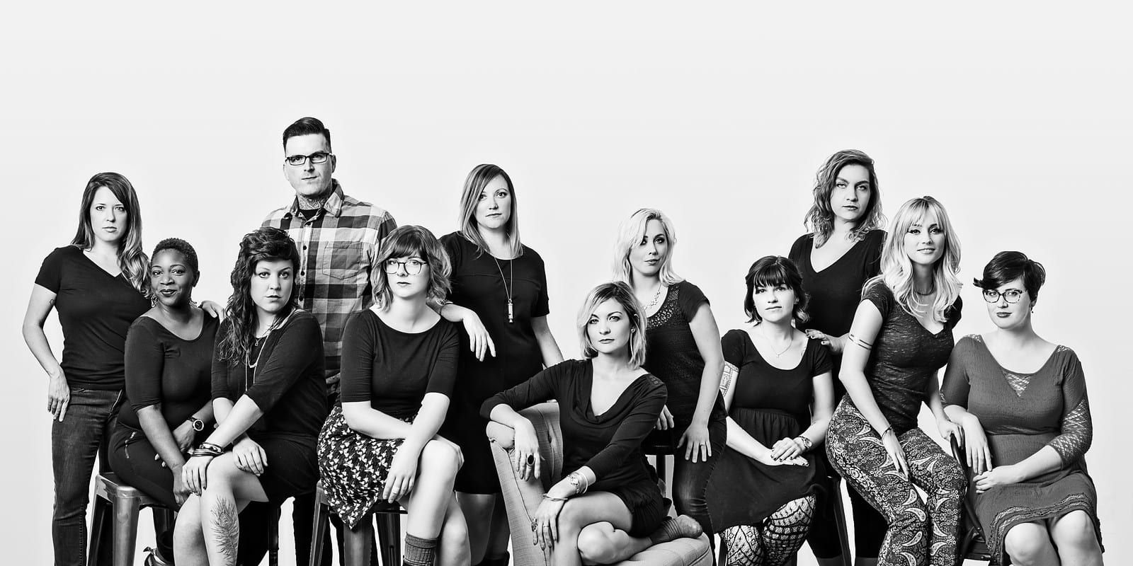 Group portrait of 13 people, black and white, studio setting. Men and women, various ages, seated and standing.