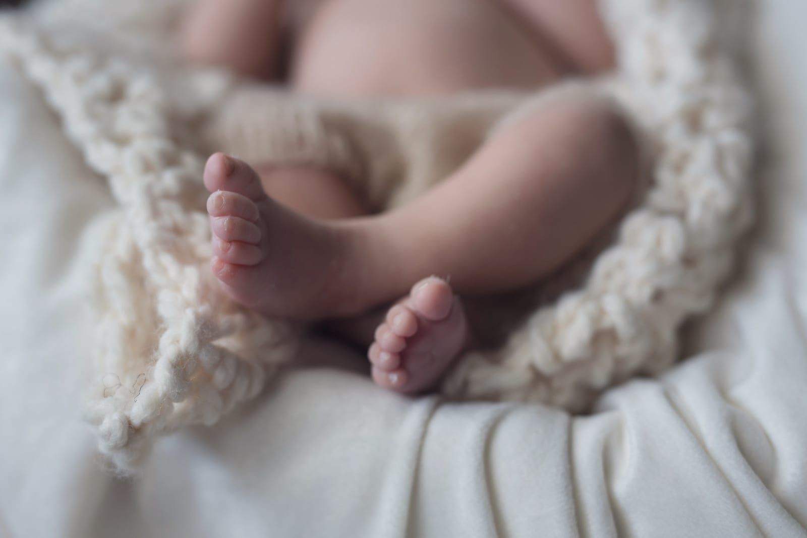 Baby's crossed feet, close-up. Soft skin, nestled in a white knitted blanket.