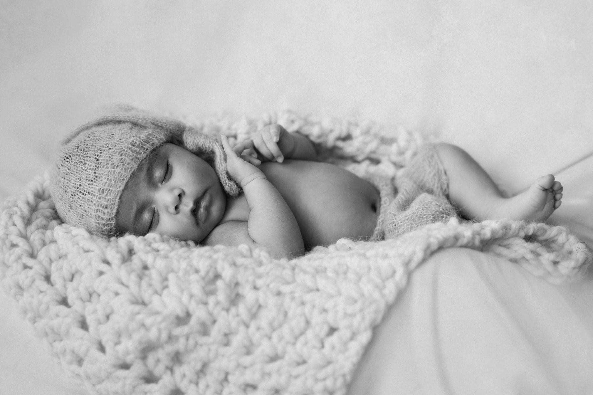 Newborn baby sleeping, wrapped in a cream-colored crocheted blanket and hat.