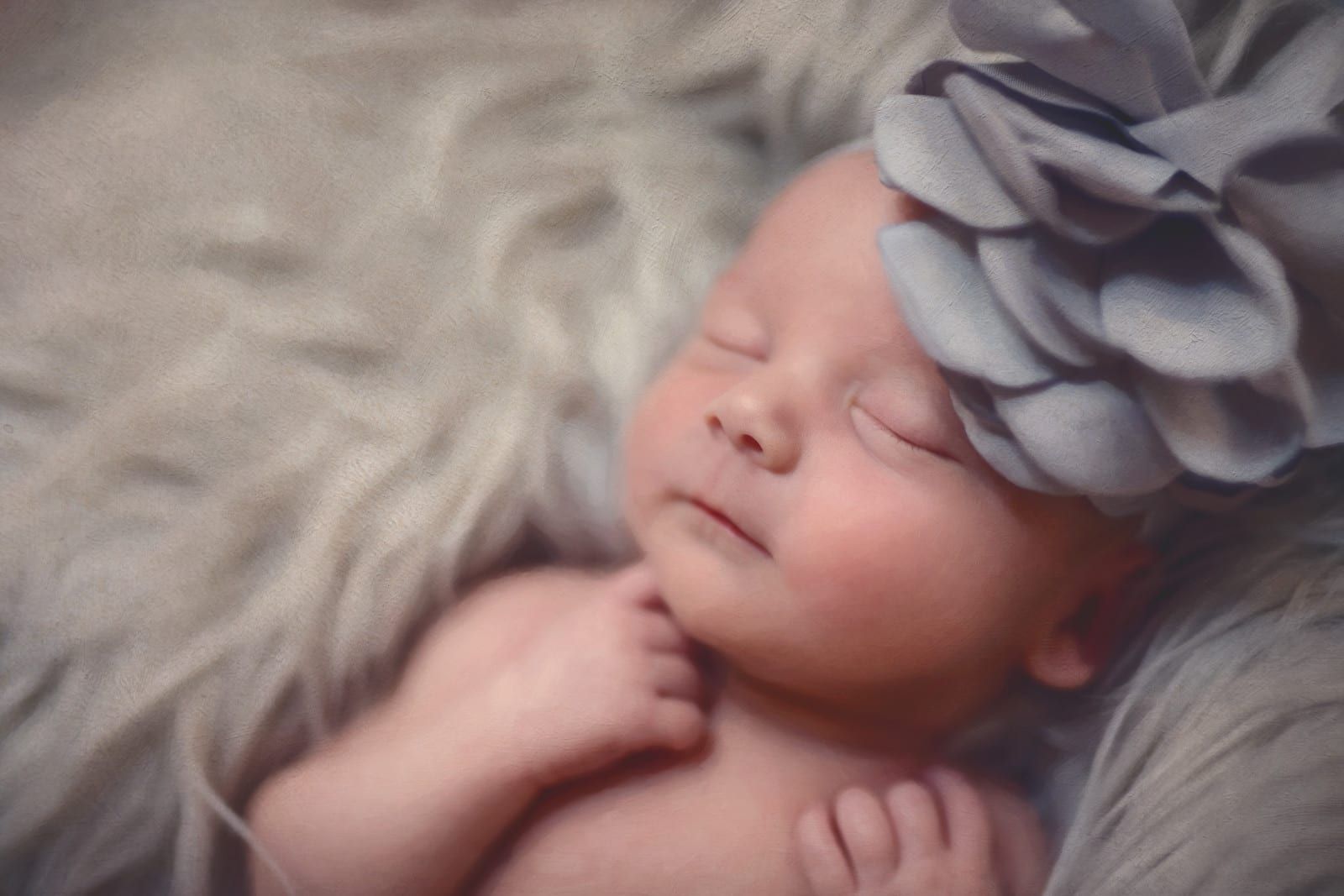 Newborn baby sleeping peacefully on fluffy gray faux fur, wearing a gray flower headband.