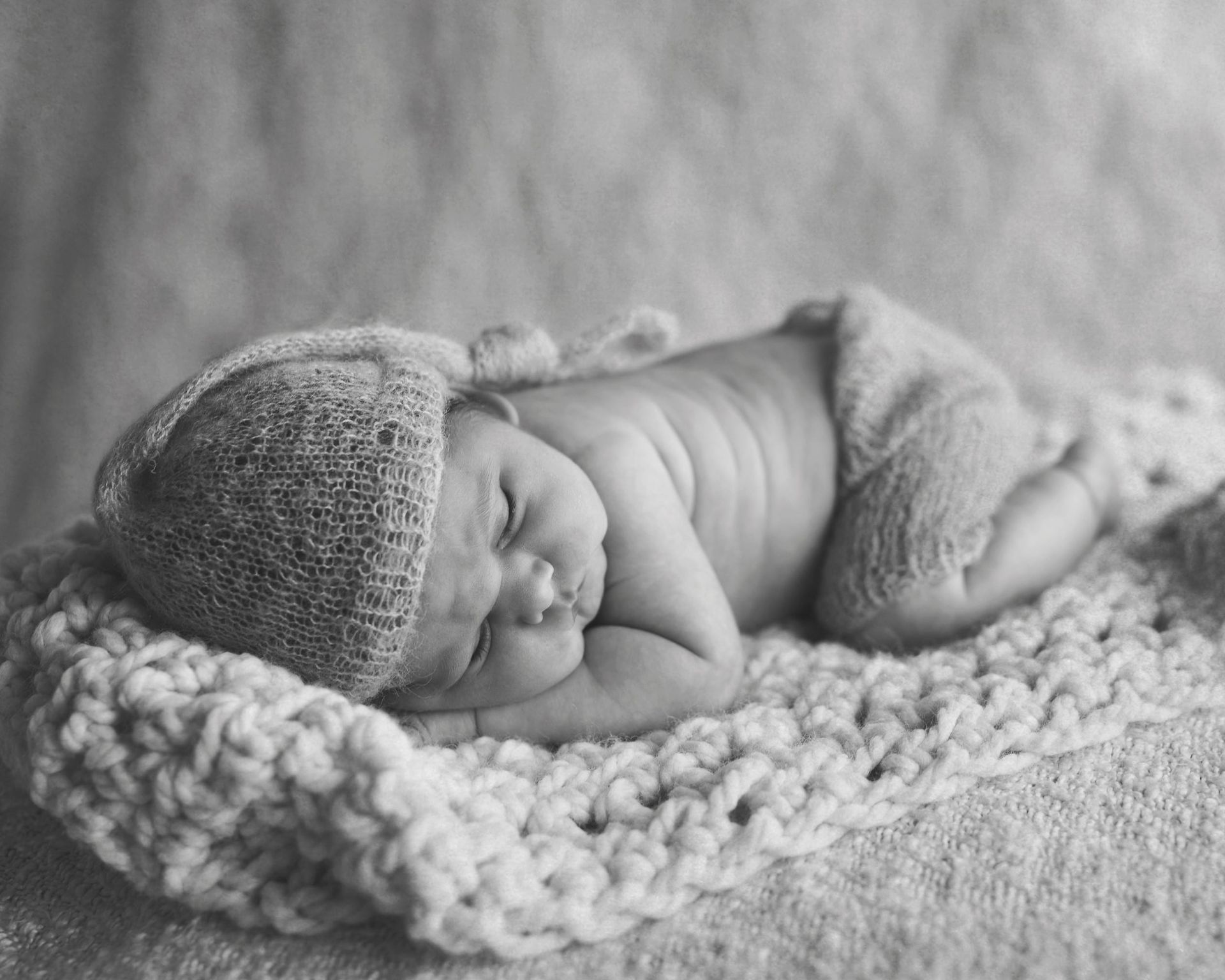 Newborn baby sleeping, wearing knit hat and diaper cover, on a crocheted blanket.