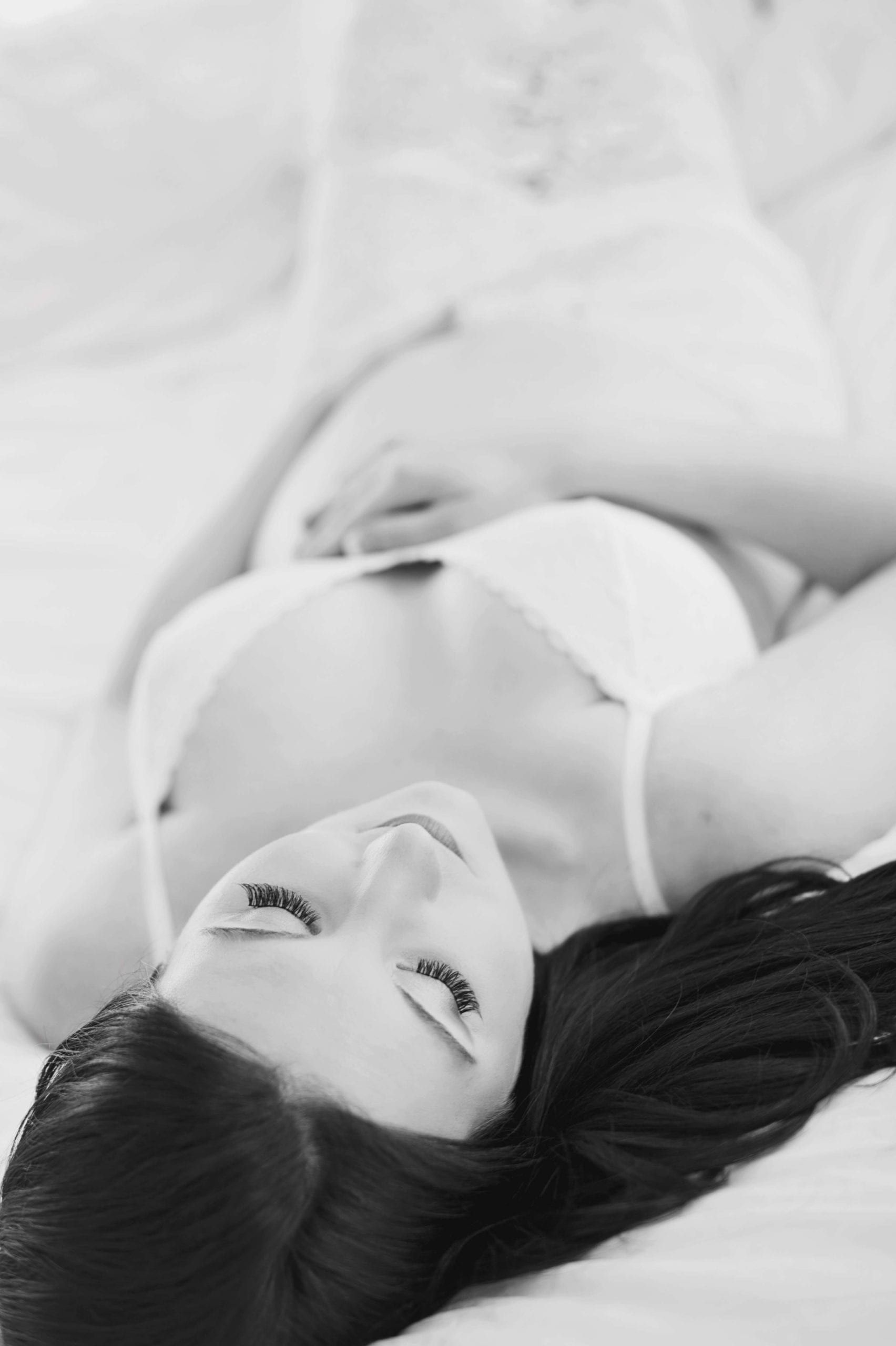 Woman lying on bed, wearing lingerie, looking at viewer, black and white.