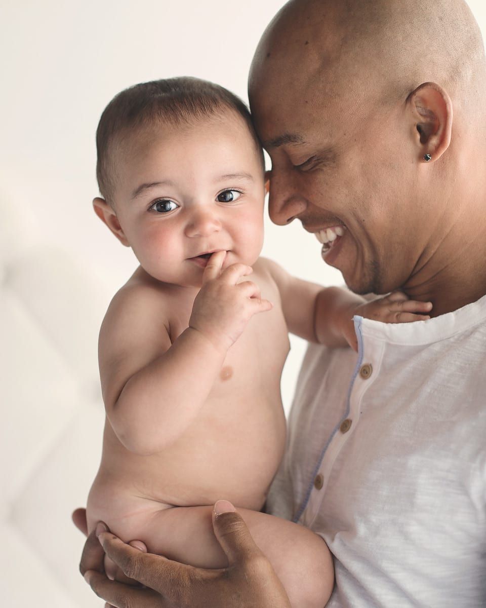 Man smiling, holding a smiling baby, both against a white background.
