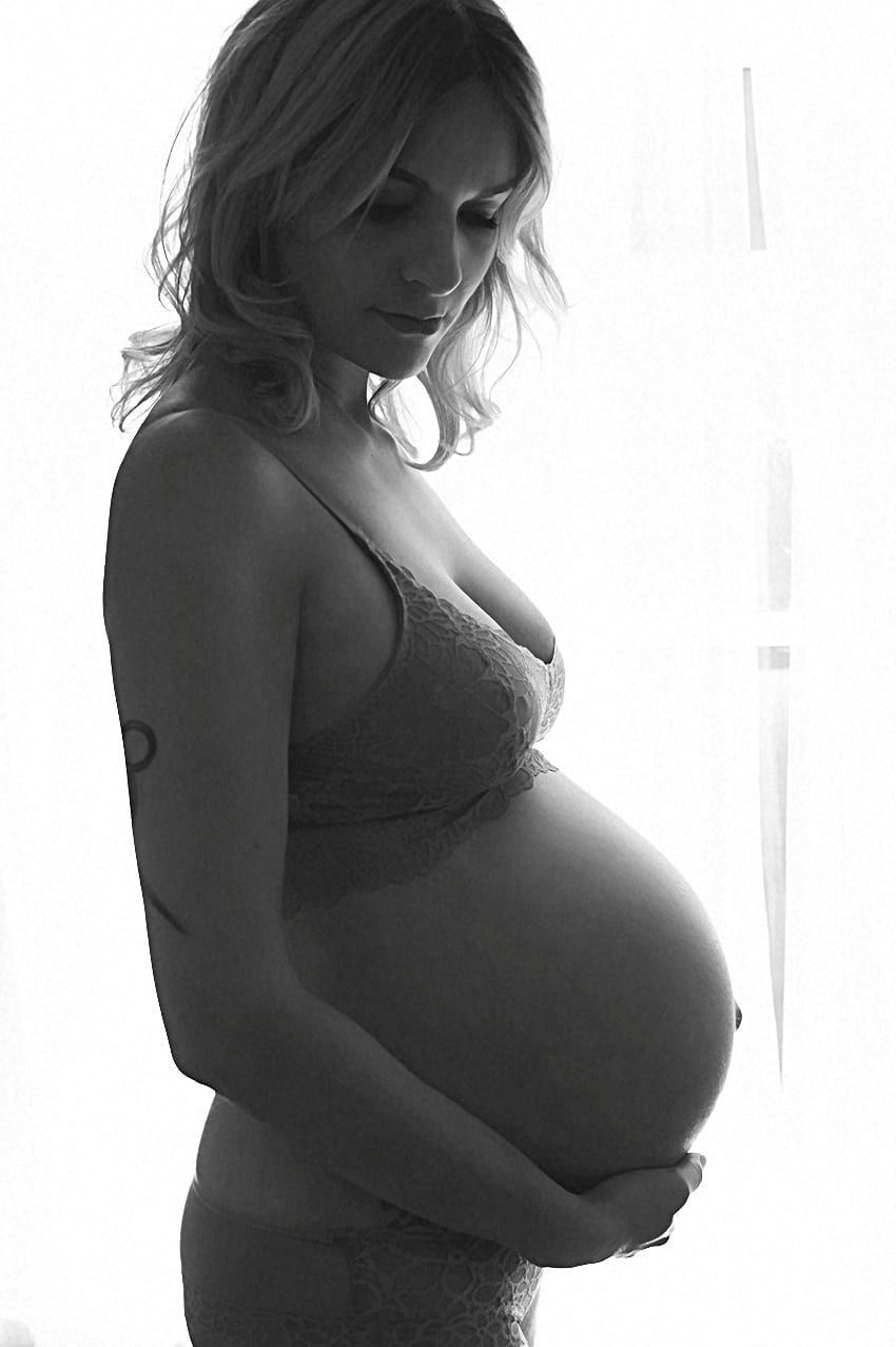 Pregnant woman in bra, holding her belly, looking down, black and white.