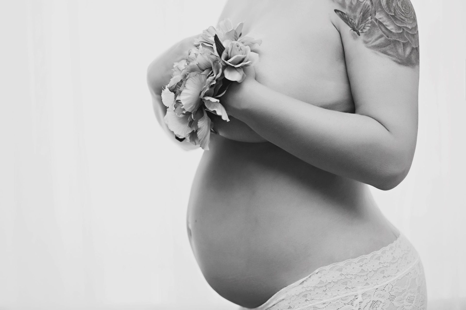 Pregnant person holding flowers, belly exposed. Black and white photo, white underwear.