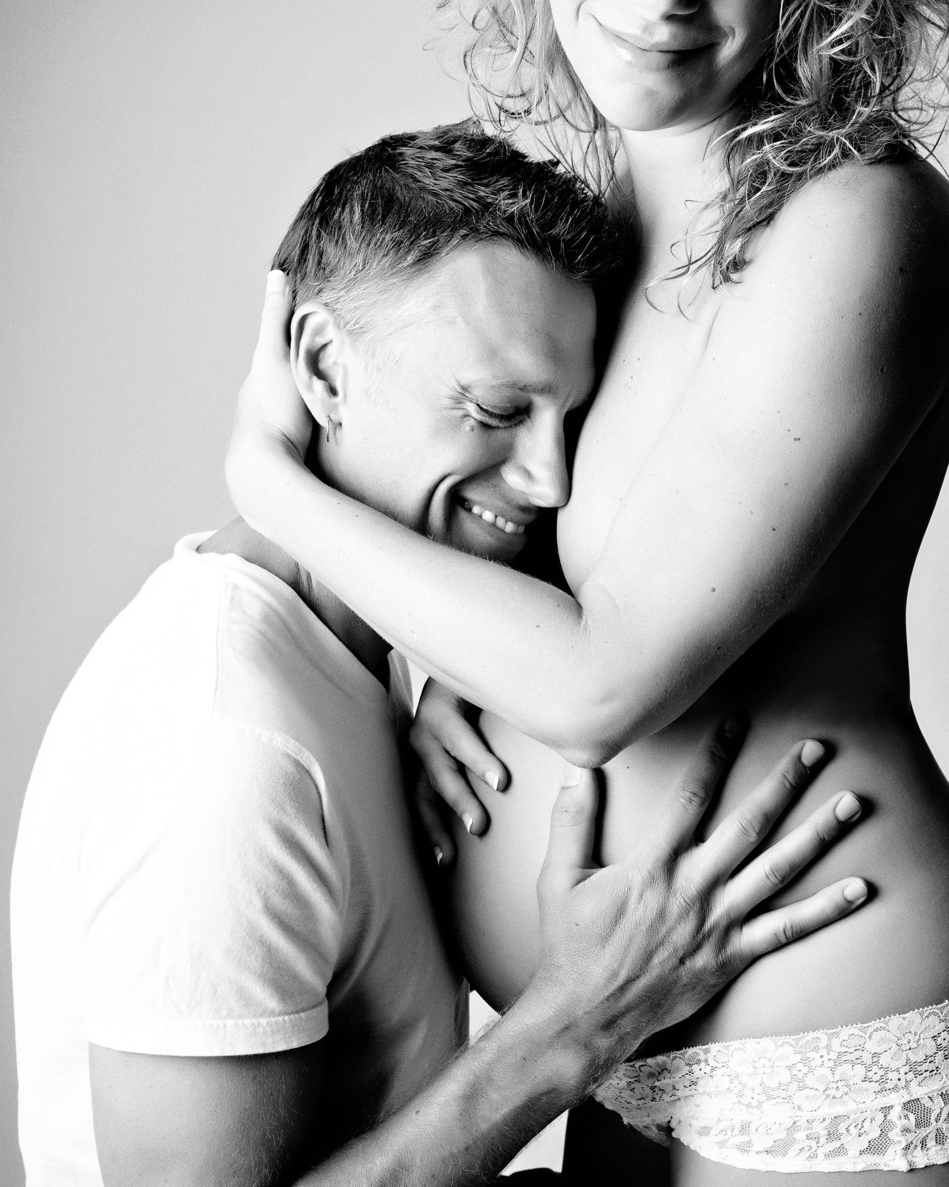 Man embraces pregnant woman, listening to her belly; black and white.