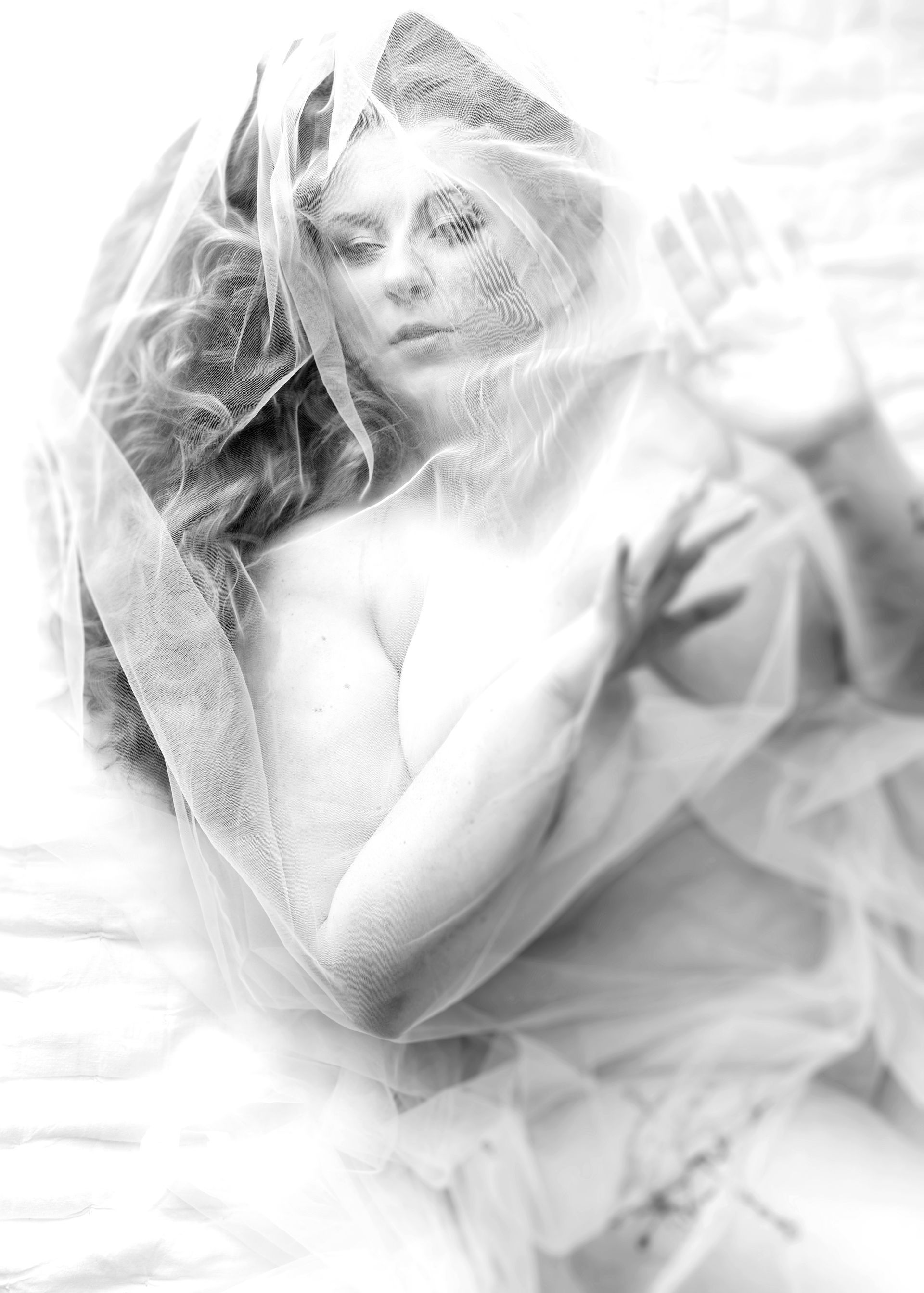 Woman with curly hair, veiled and partially nude, reaches toward the viewer. Black and white.