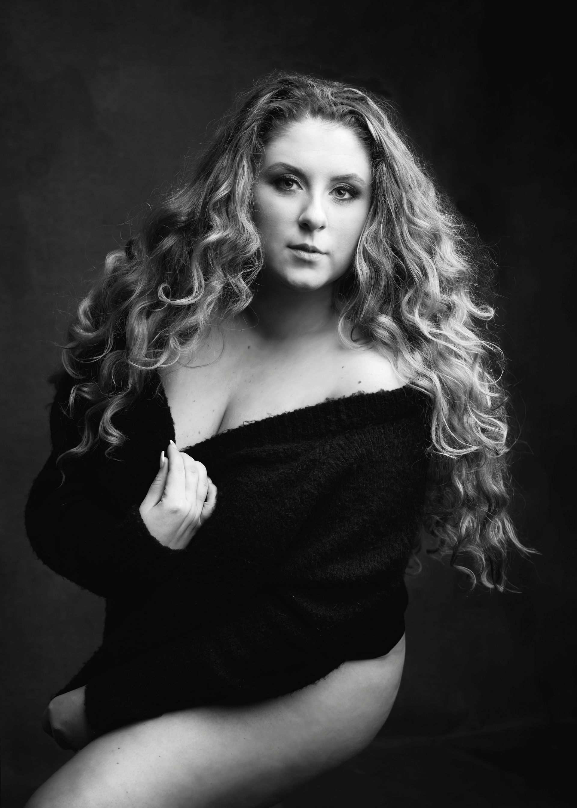 Woman with long curly hair in a black sweater, looking at the camera in a studio setting.