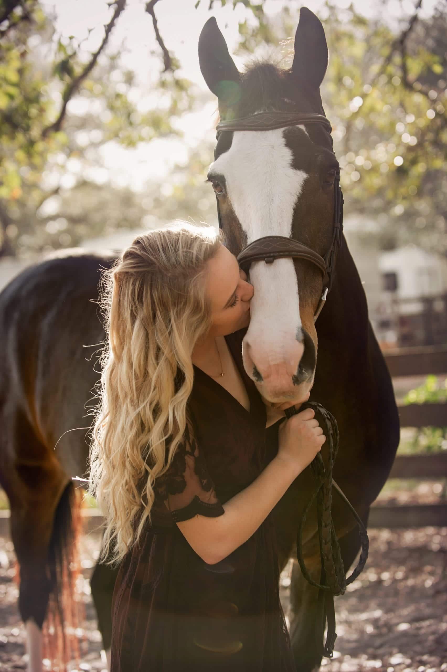 Woman in black dress kisses a brown and white horse outdoors.