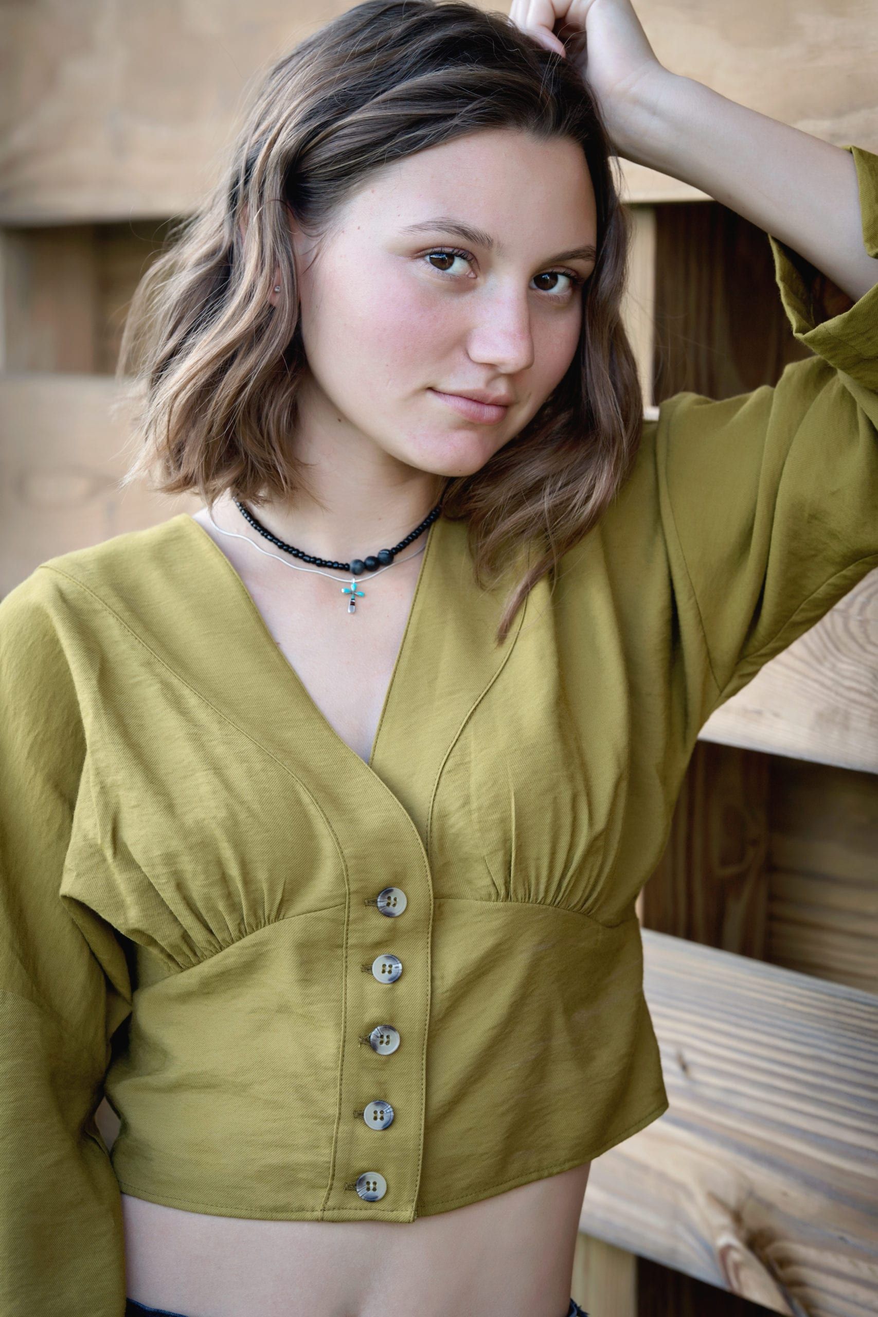 Woman with short brown hair in green blouse, hand on head, looking at camera.
