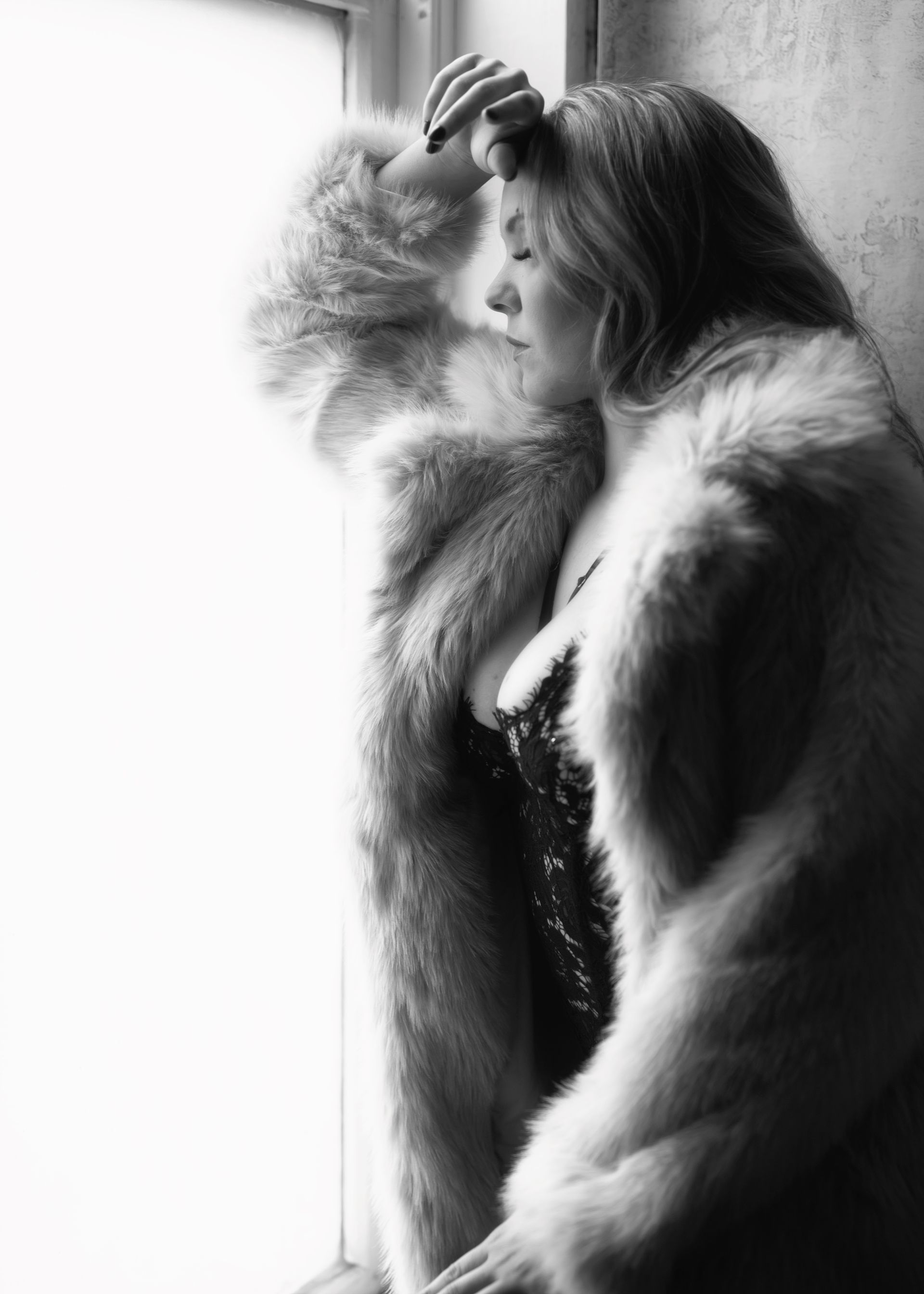 Woman in fur coat leaning against a window, face in shadow. Black and white photo.