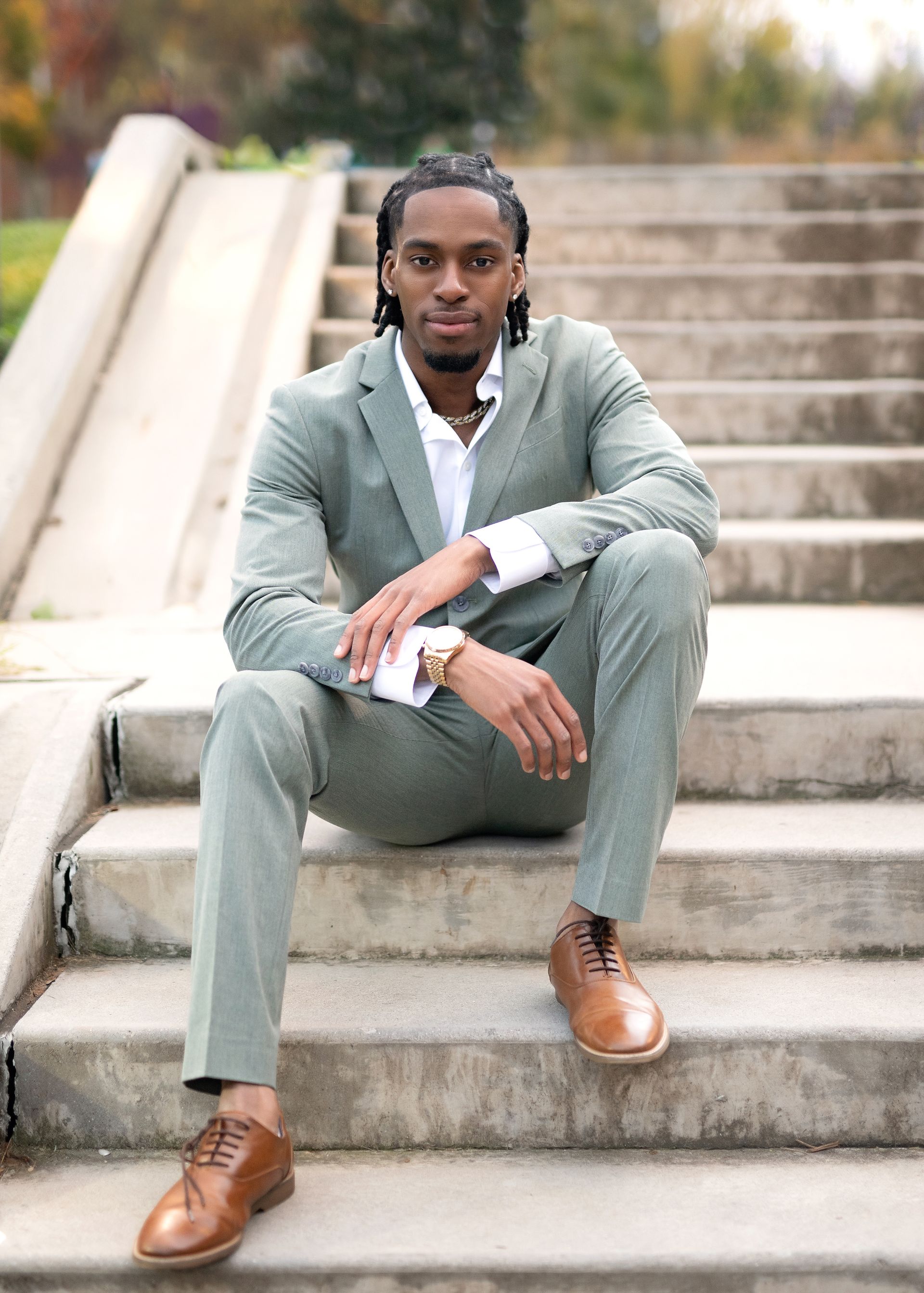 Man in green suit sits on concrete stairs, brown shoes.