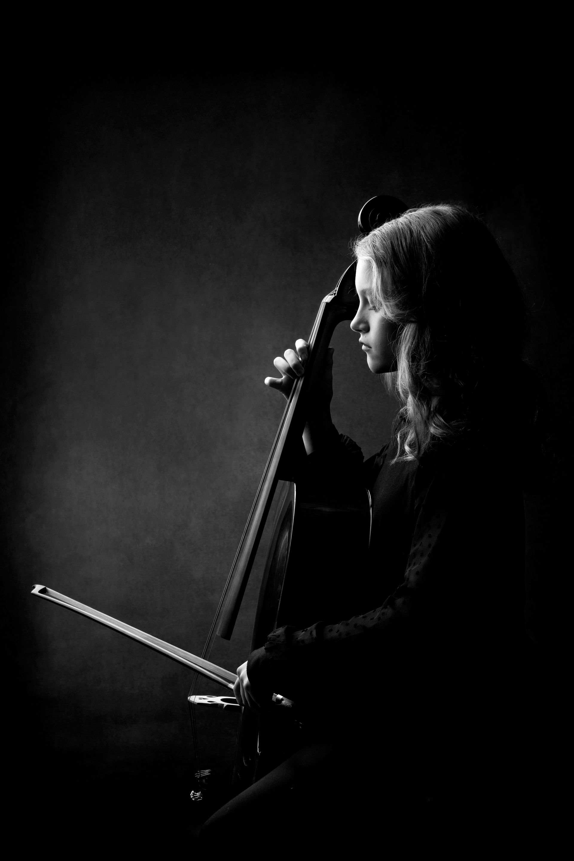 Cellist in profile, playing cello, in a dim setting. Black and white.
