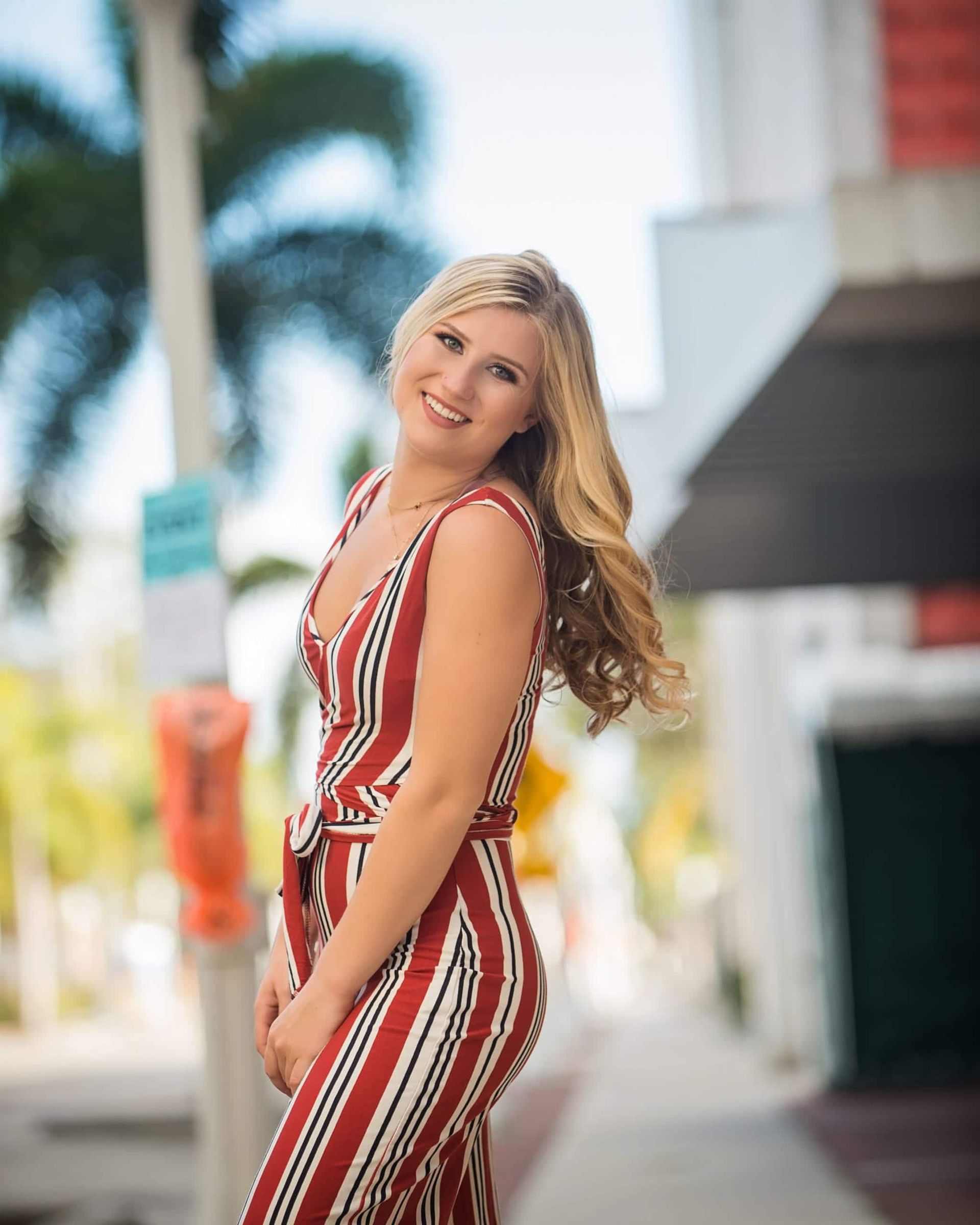 Blonde woman in a red and white striped jumpsuit smiles outdoors.