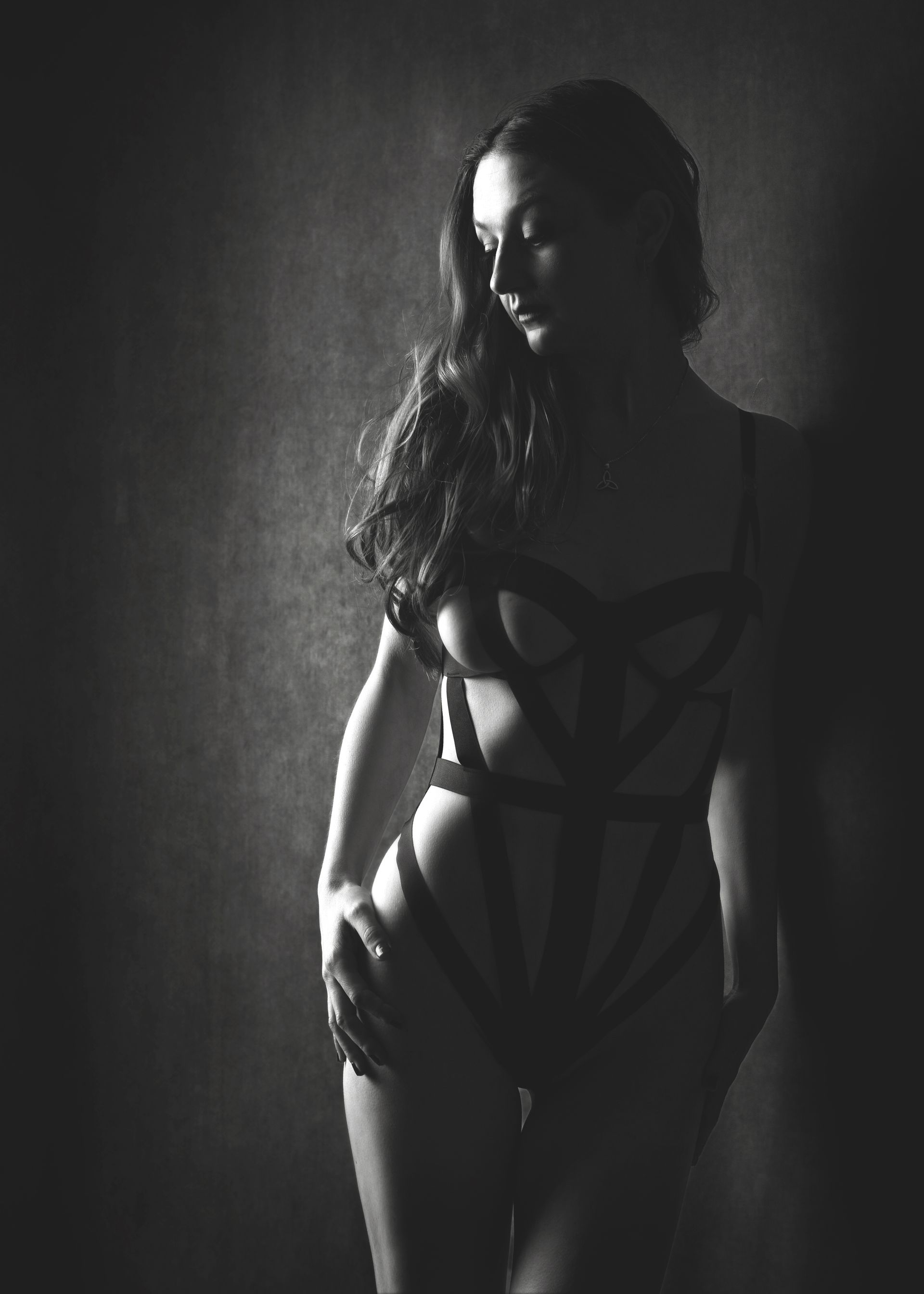 Woman in lingerie, leaning against wall. Black and white, shadowy lighting.