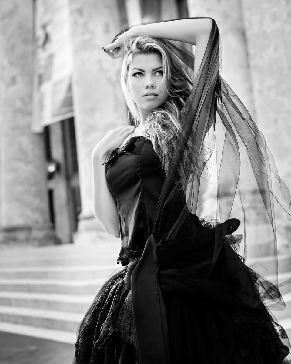 Woman in black dress poses dramatically outdoors, hair blowing.