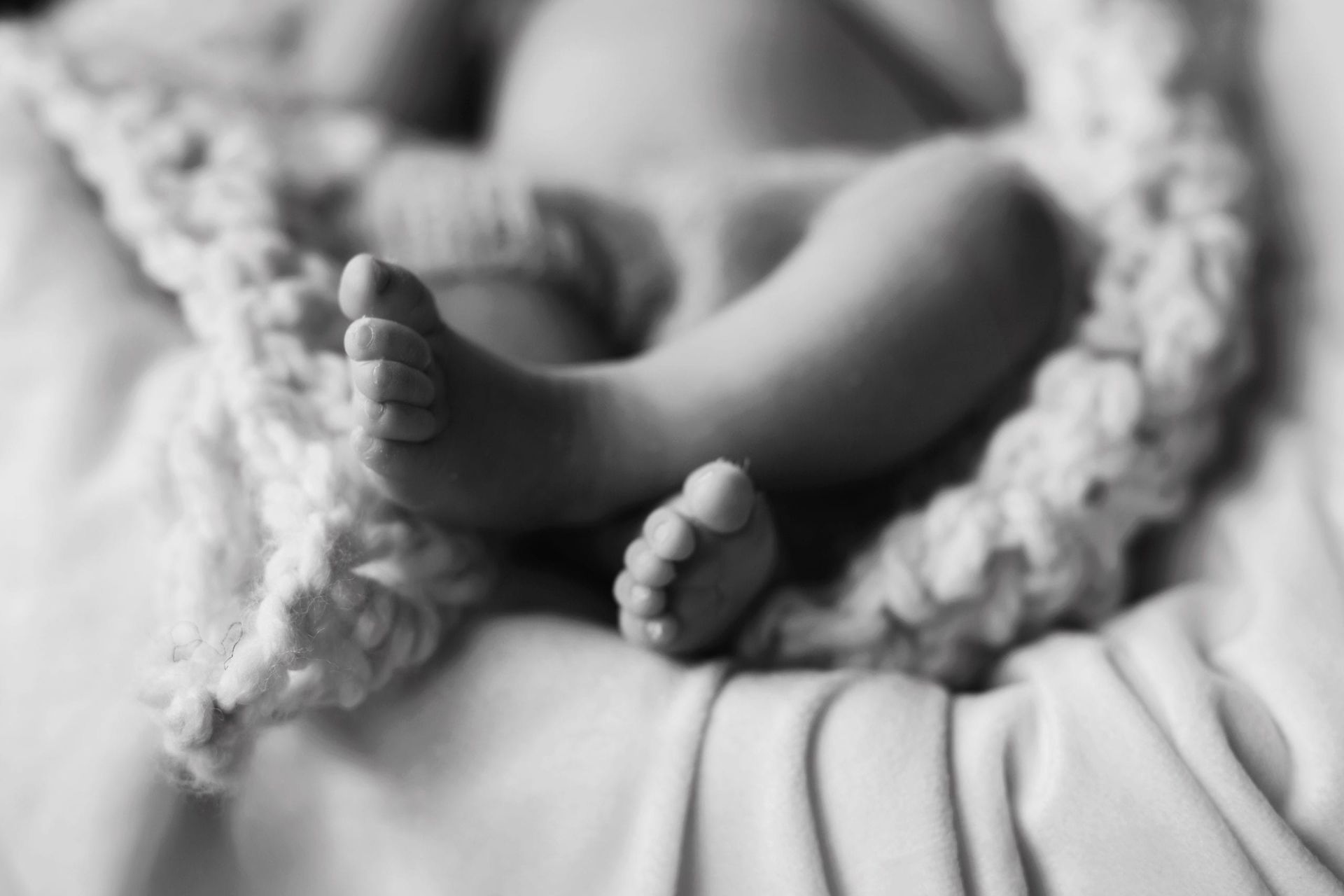Baby's crossed feet, resting on a cream-colored knitted blanket. Black and white.