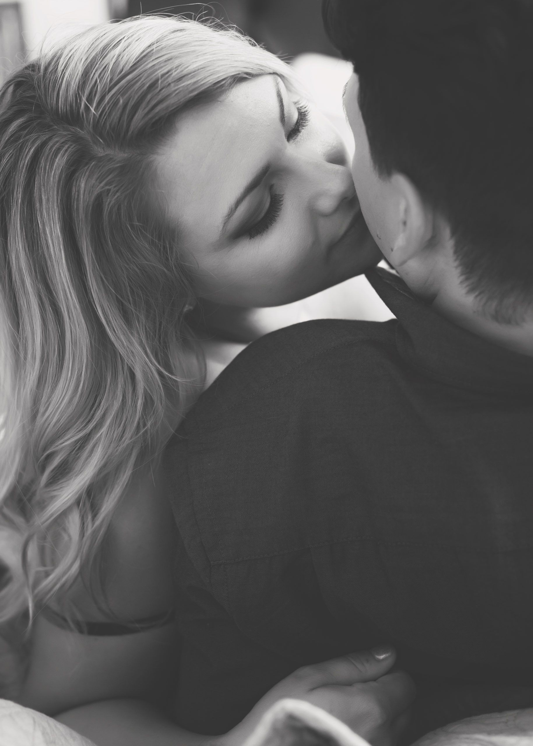 Woman kissing a man on the cheek; both are close together in a romantic embrace.