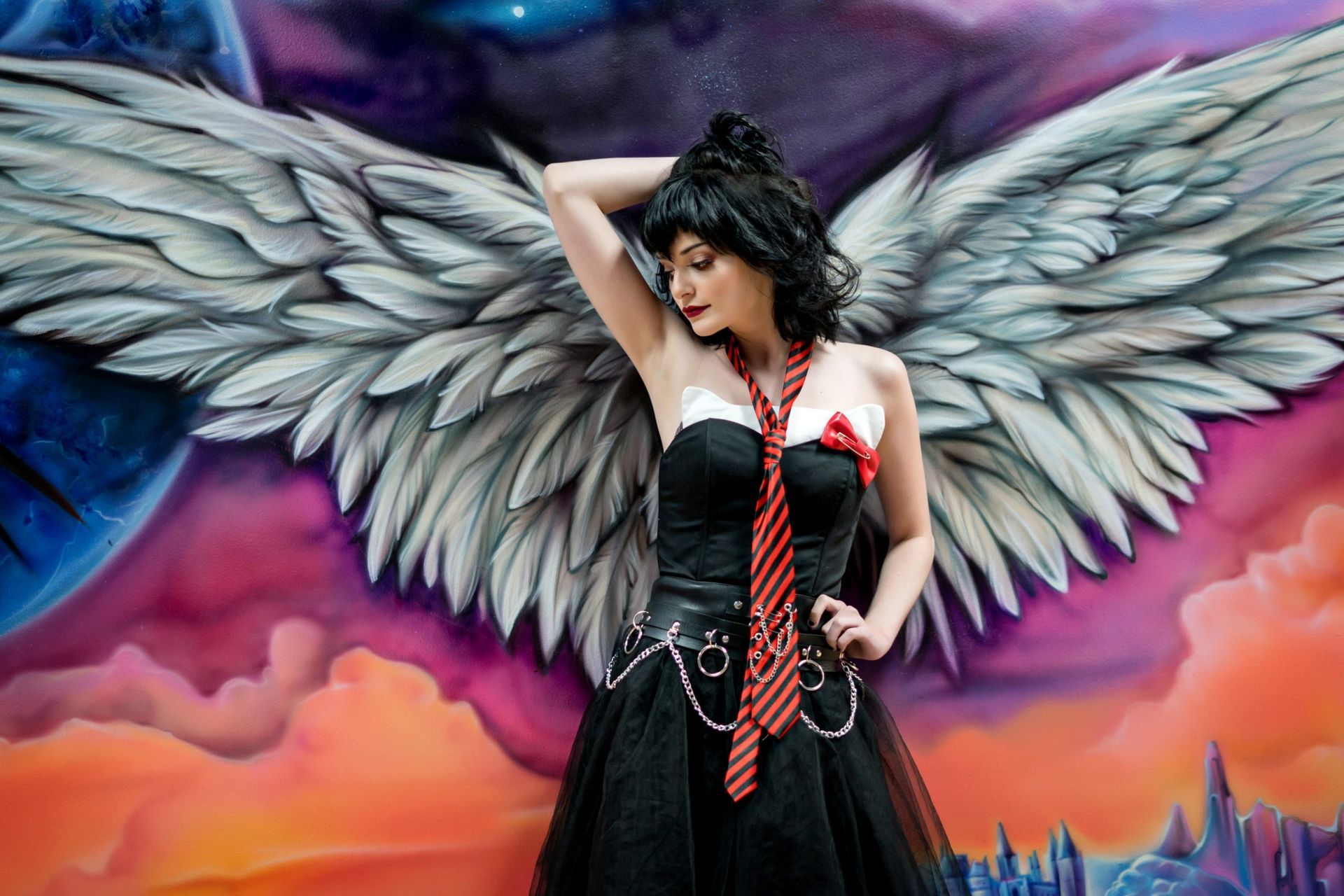 Woman in black dress and angel wings poses against a colorful mural.