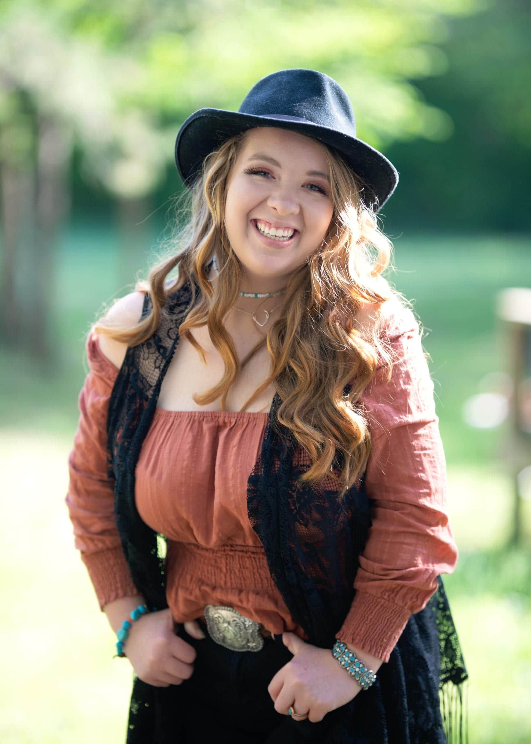 Woman in hat and vest smiles outdoors.
