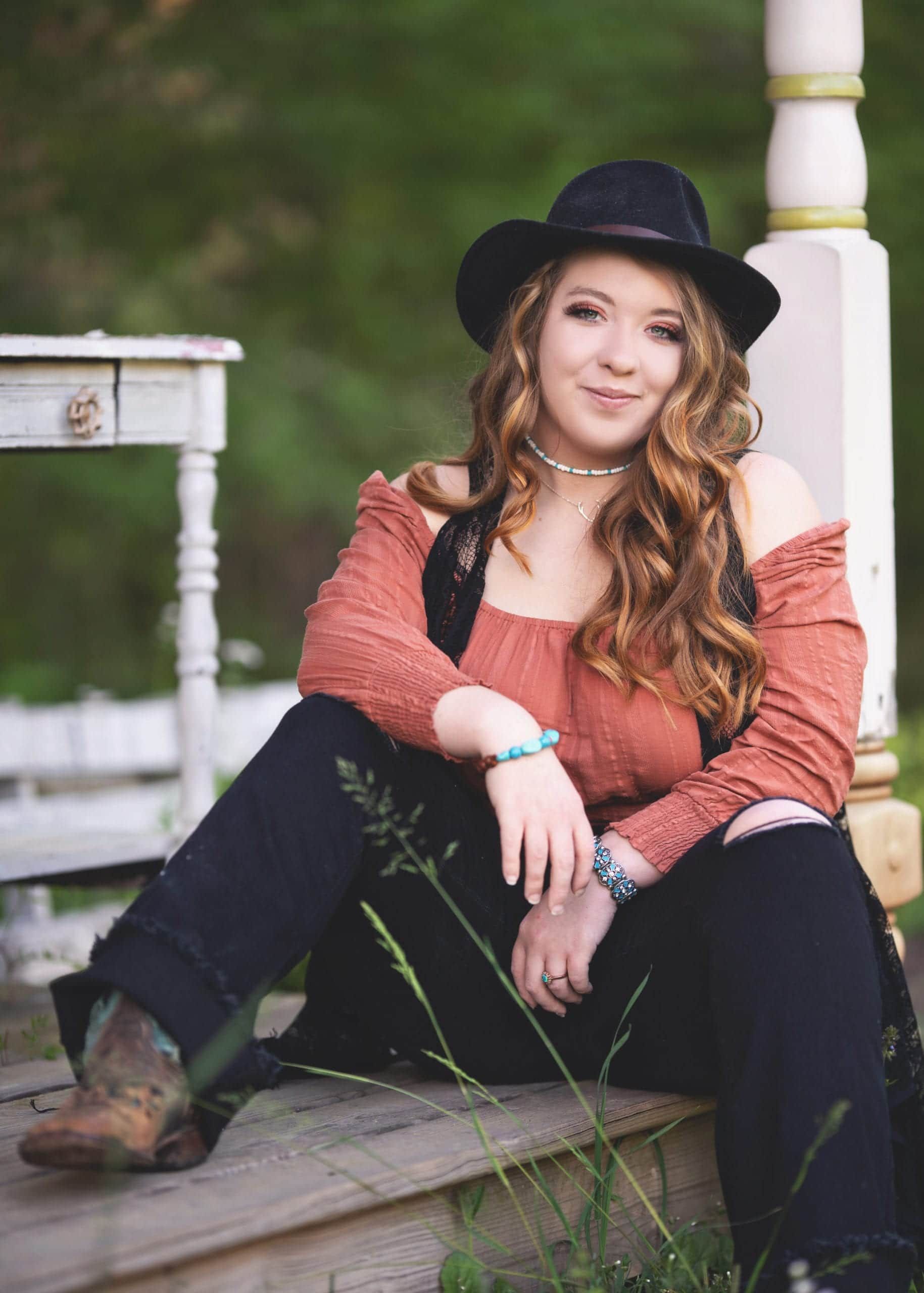 Woman in a cowboy hat, orange top, and boots, sitting on porch steps.