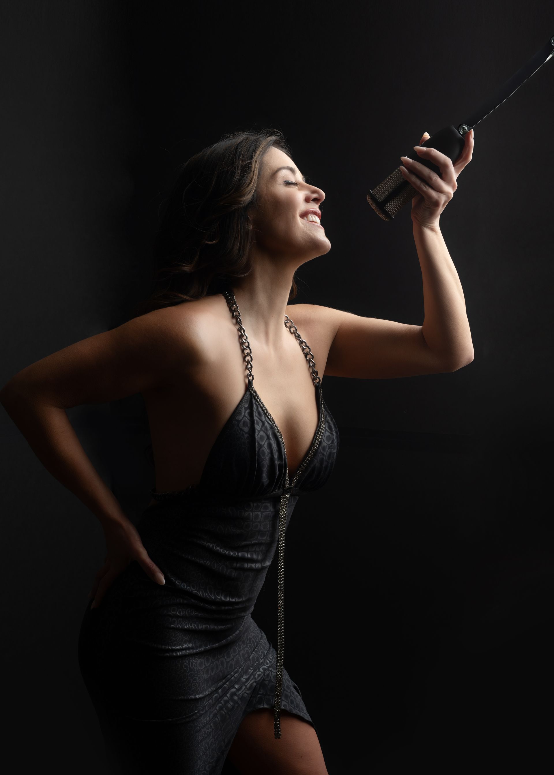 Woman in black dress, smiling, holding up a bottle of champagne against a dark background.