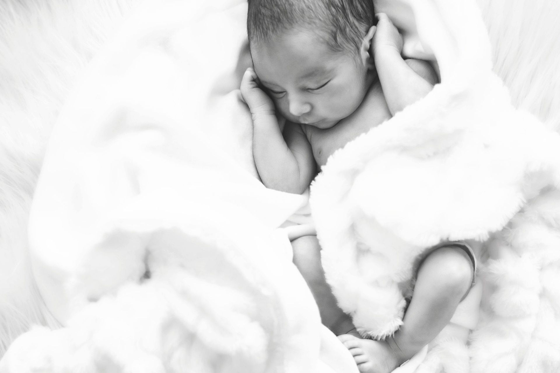 Newborn baby sleeping, wrapped in a soft, white blanket.