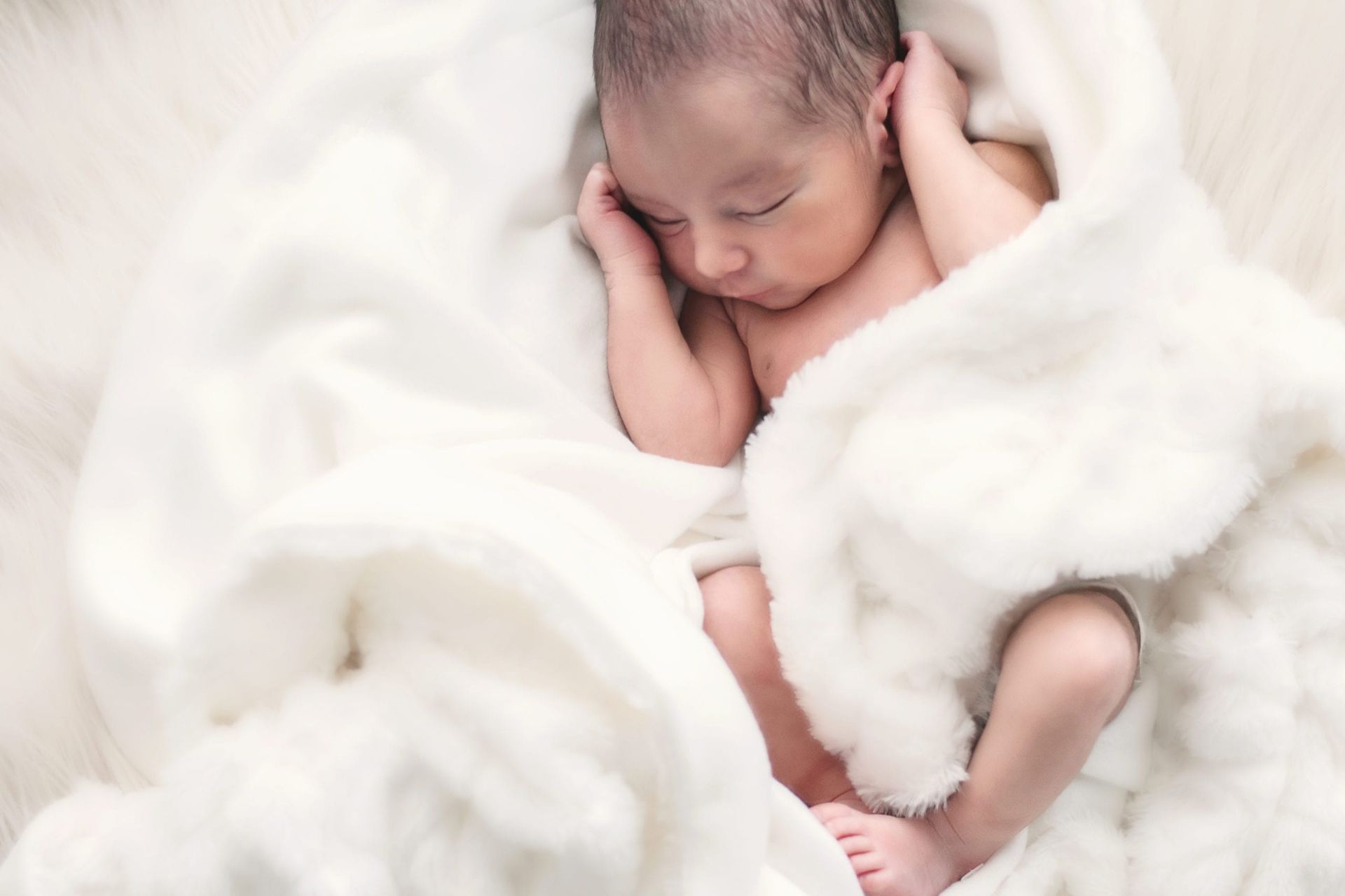 Newborn baby sleeping peacefully, wrapped in a soft, white blanket.