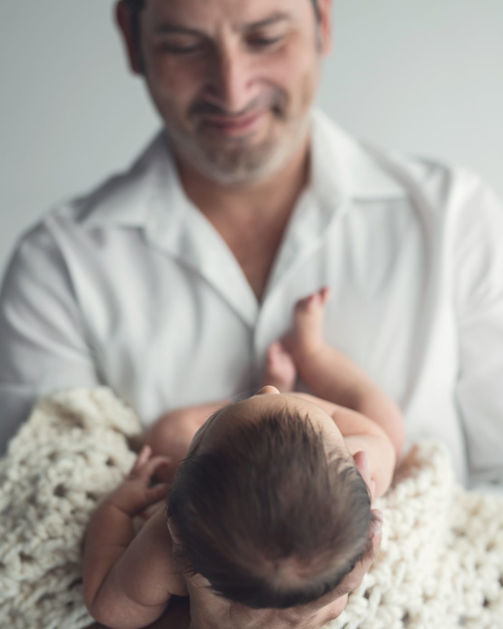 Father gazing lovingly at a newborn baby lying on a cream-colored blanket.