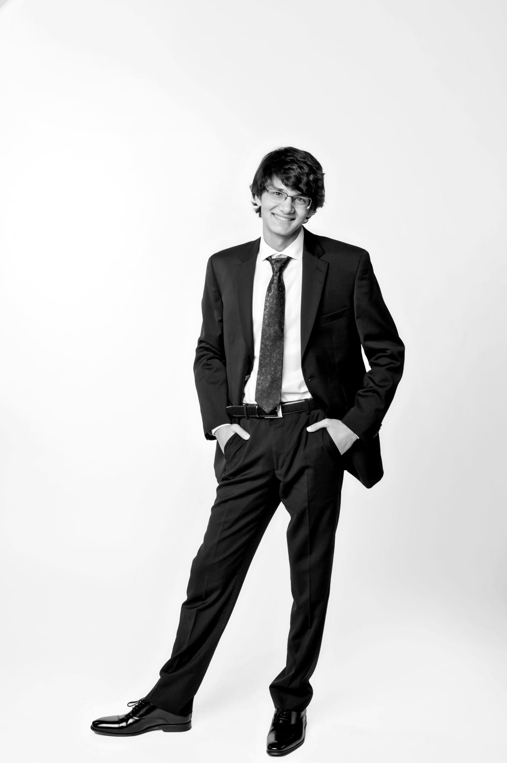 Man in suit, smiling, hands in pockets, standing against a white background.