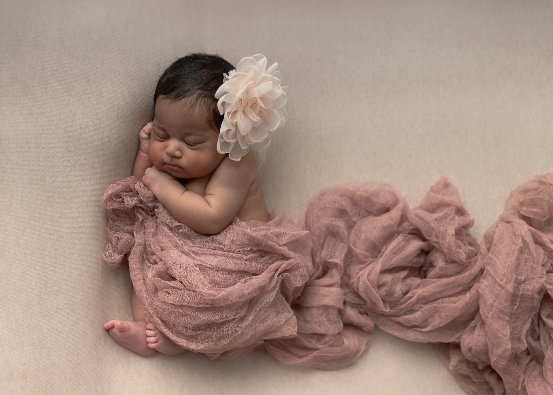 Newborn baby sleeping, wrapped in pink fabric, with a flower on its head.