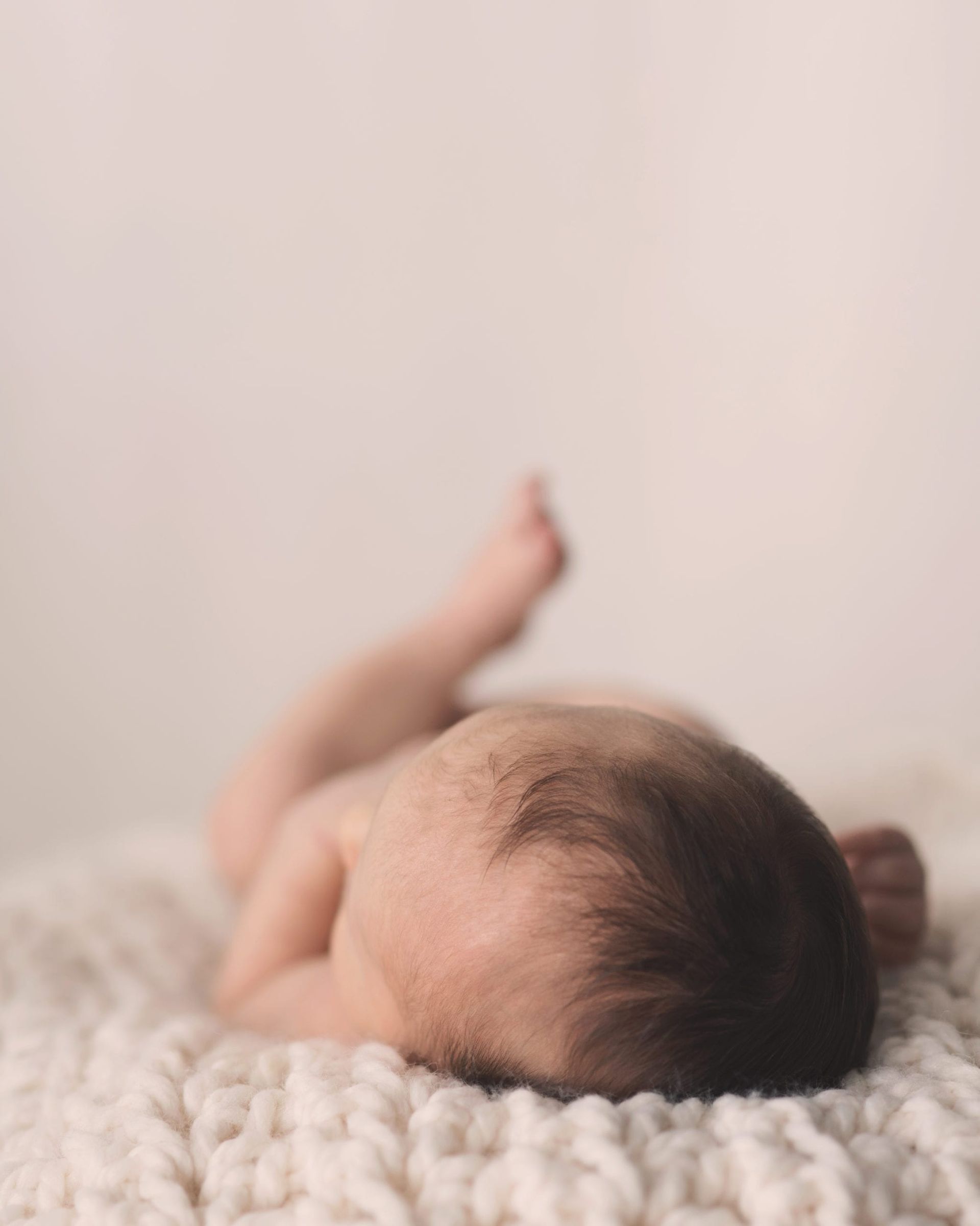 Baby lying on a white knitted blanket, back and head facing the camera.