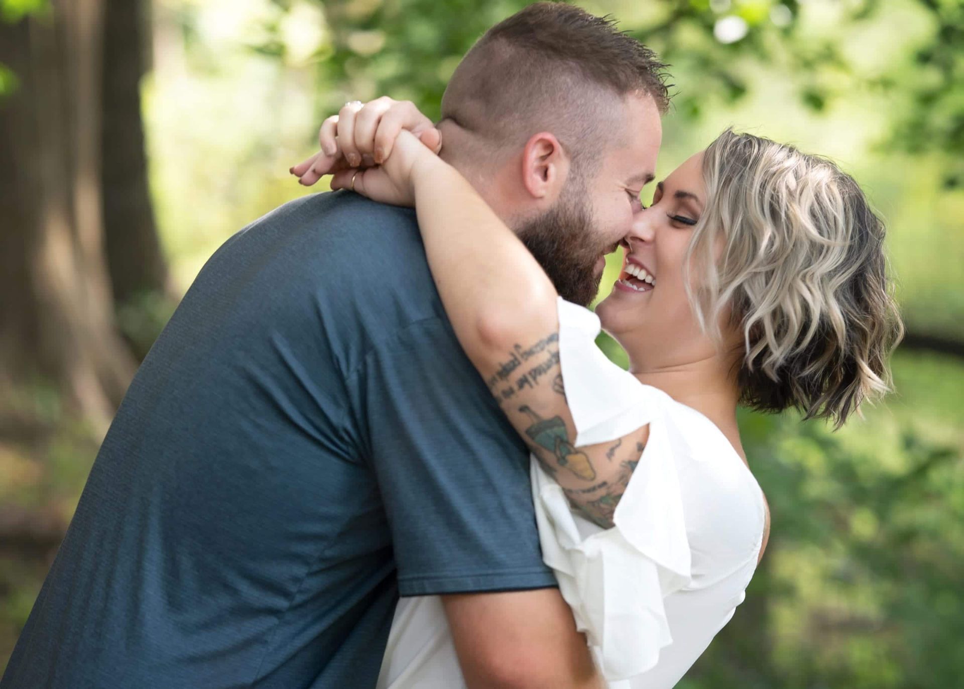 Couple embracing, smiling, laughing outdoors. Woman in white dress, man in blue shirt.