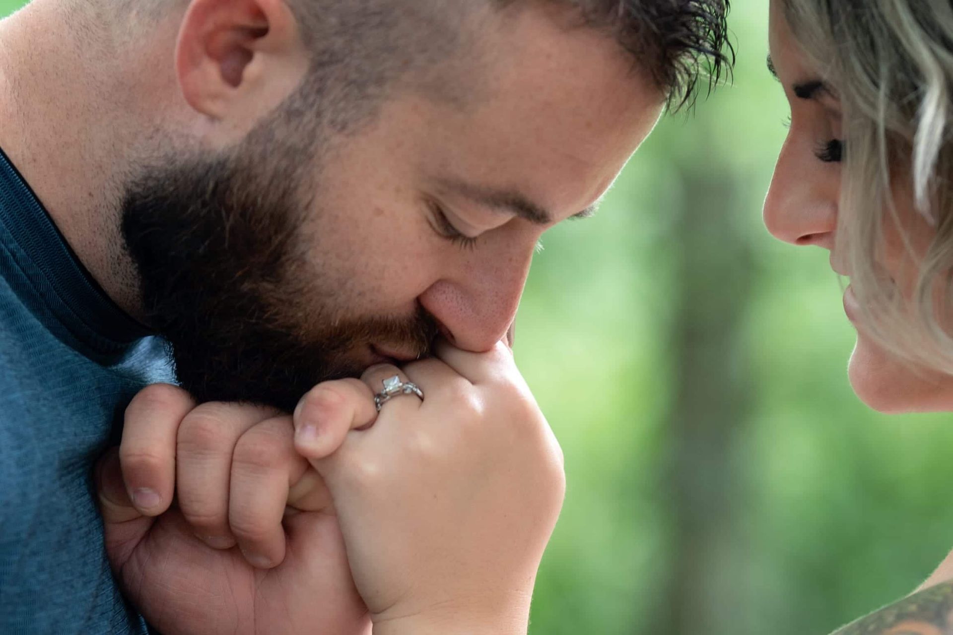 Man kissing woman's hand with engagement ring. Green bokeh background.