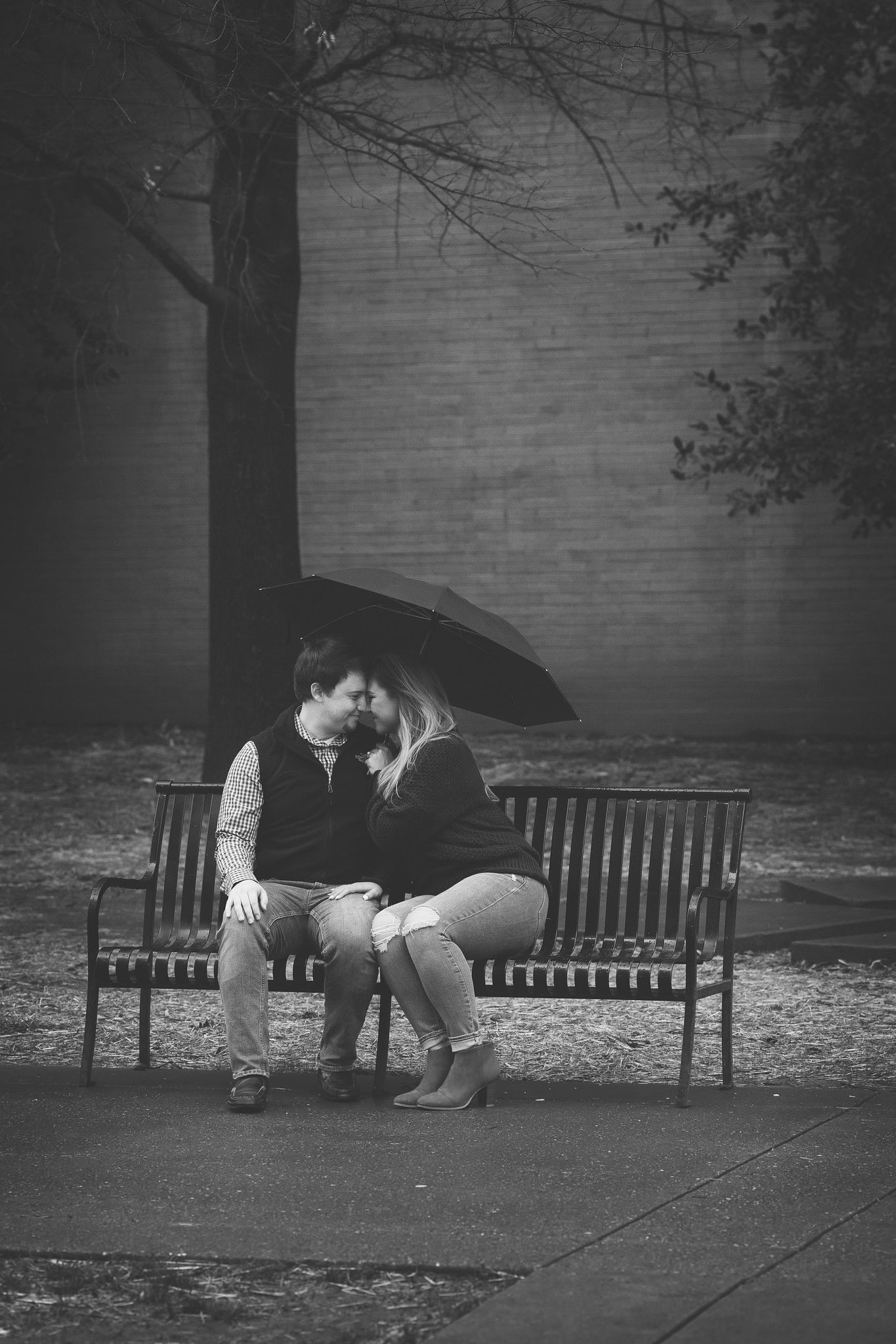 Couple under umbrella on a park bench, about to kiss. Black and white.