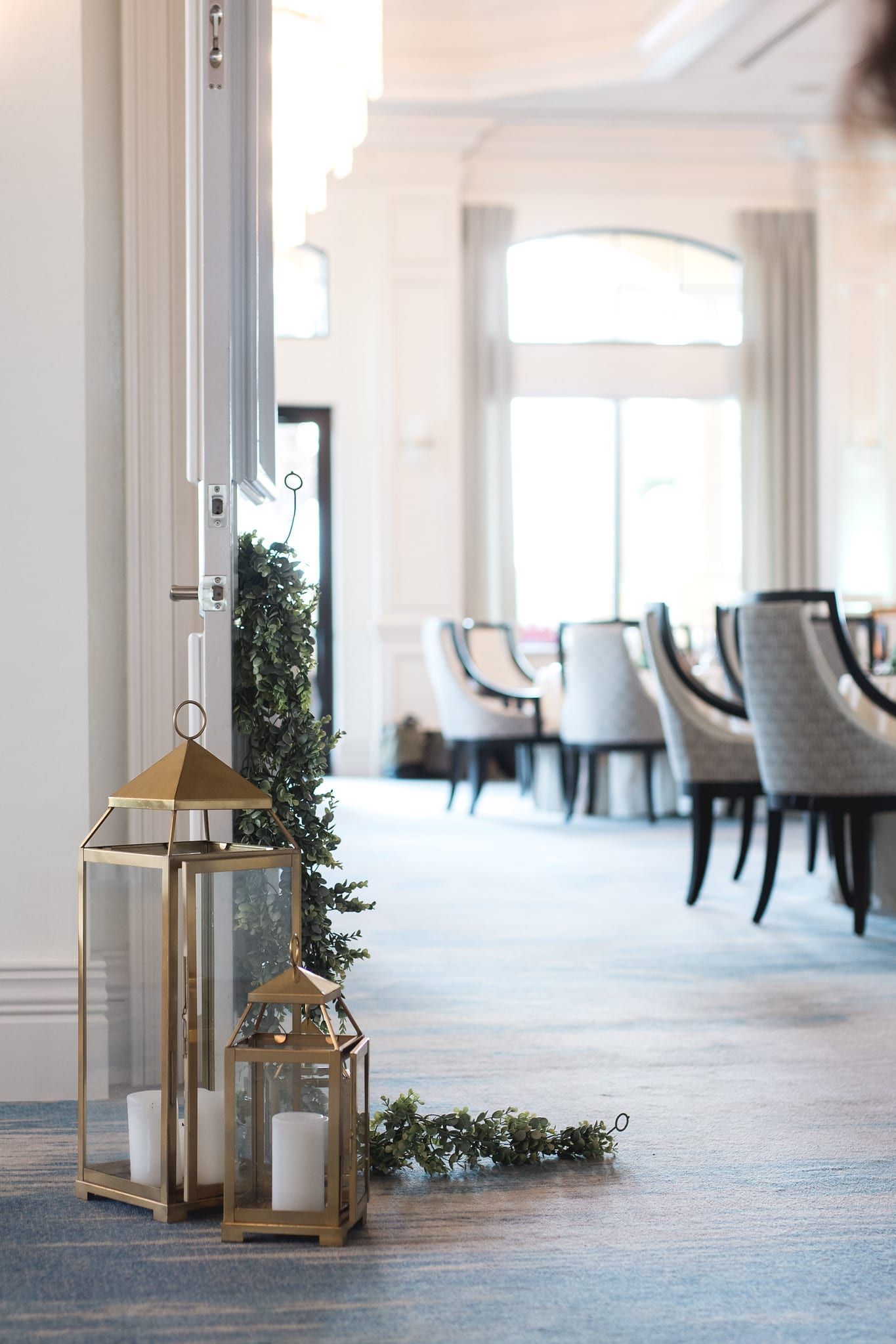 Gold lanterns with candles, greenery, and a view of a dining room with chairs.