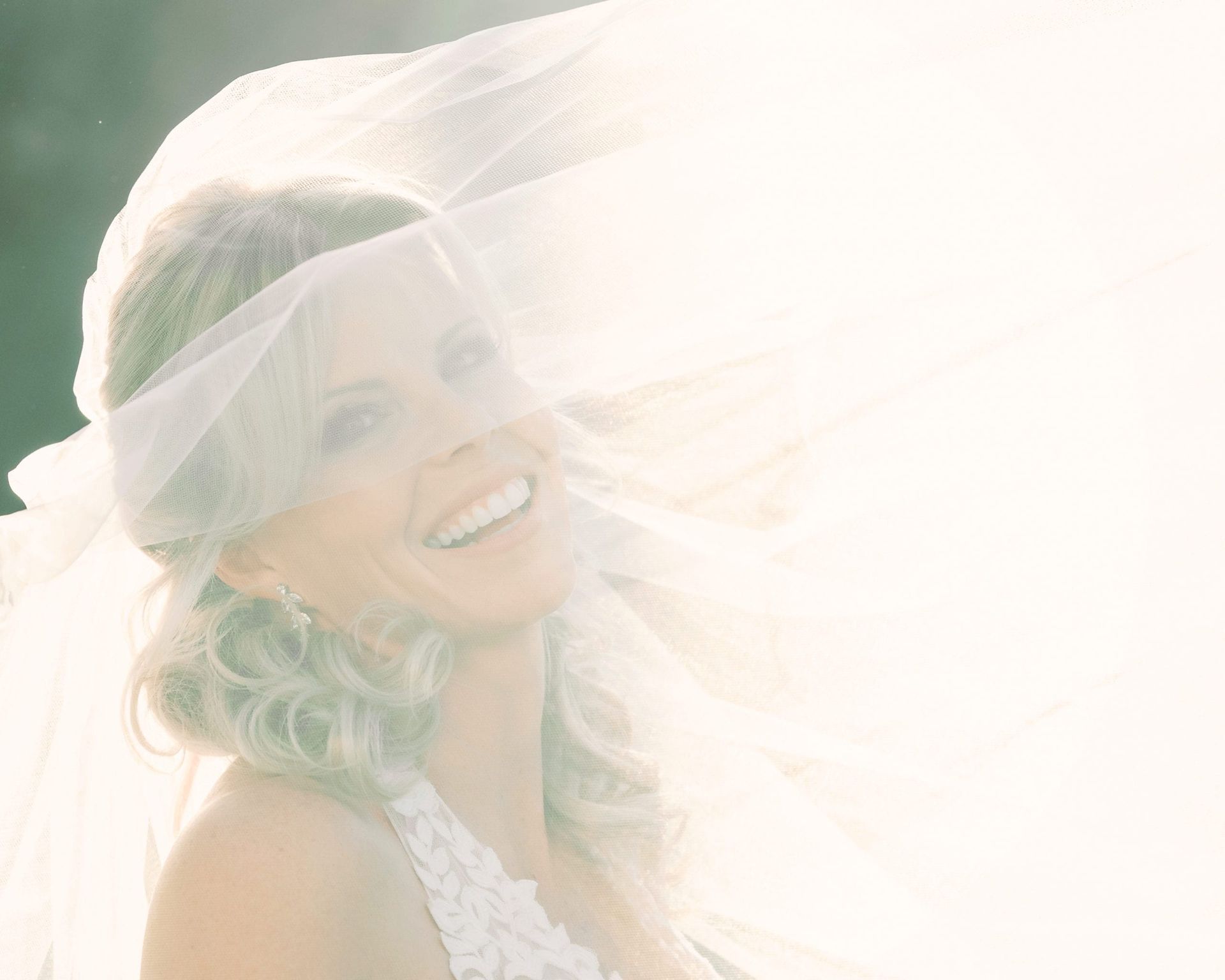 Smiling bride with veil blowing in the wind. Soft focus with bright light.