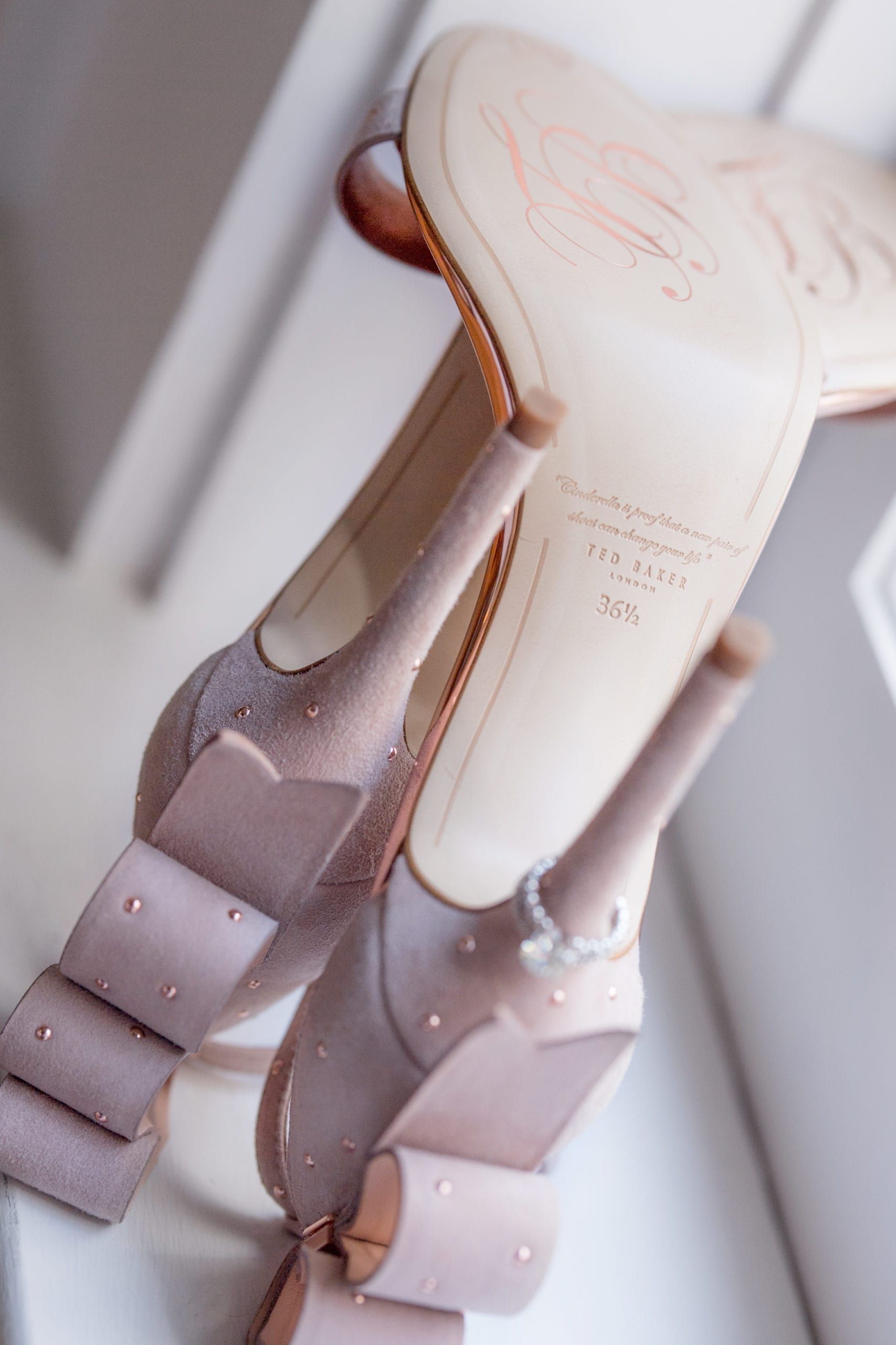 Pink high-heeled shoes with bow details, resting on a white surface, showing the undersides and heels.