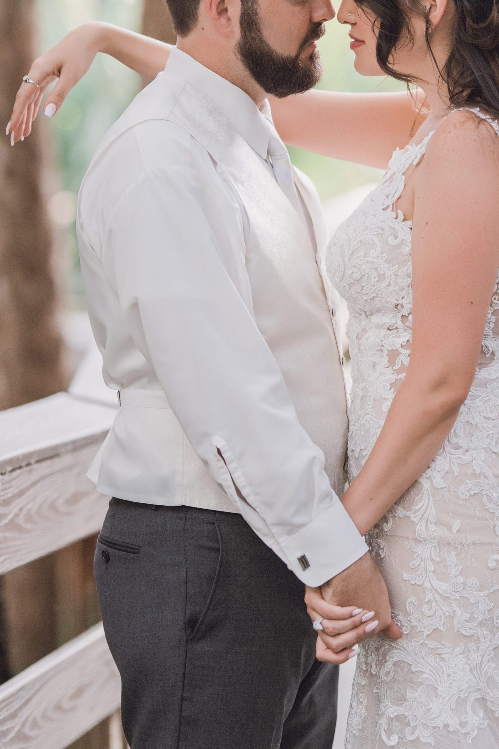 Bride and groom holding hands and embracing near a wooden railing, soft lighting.