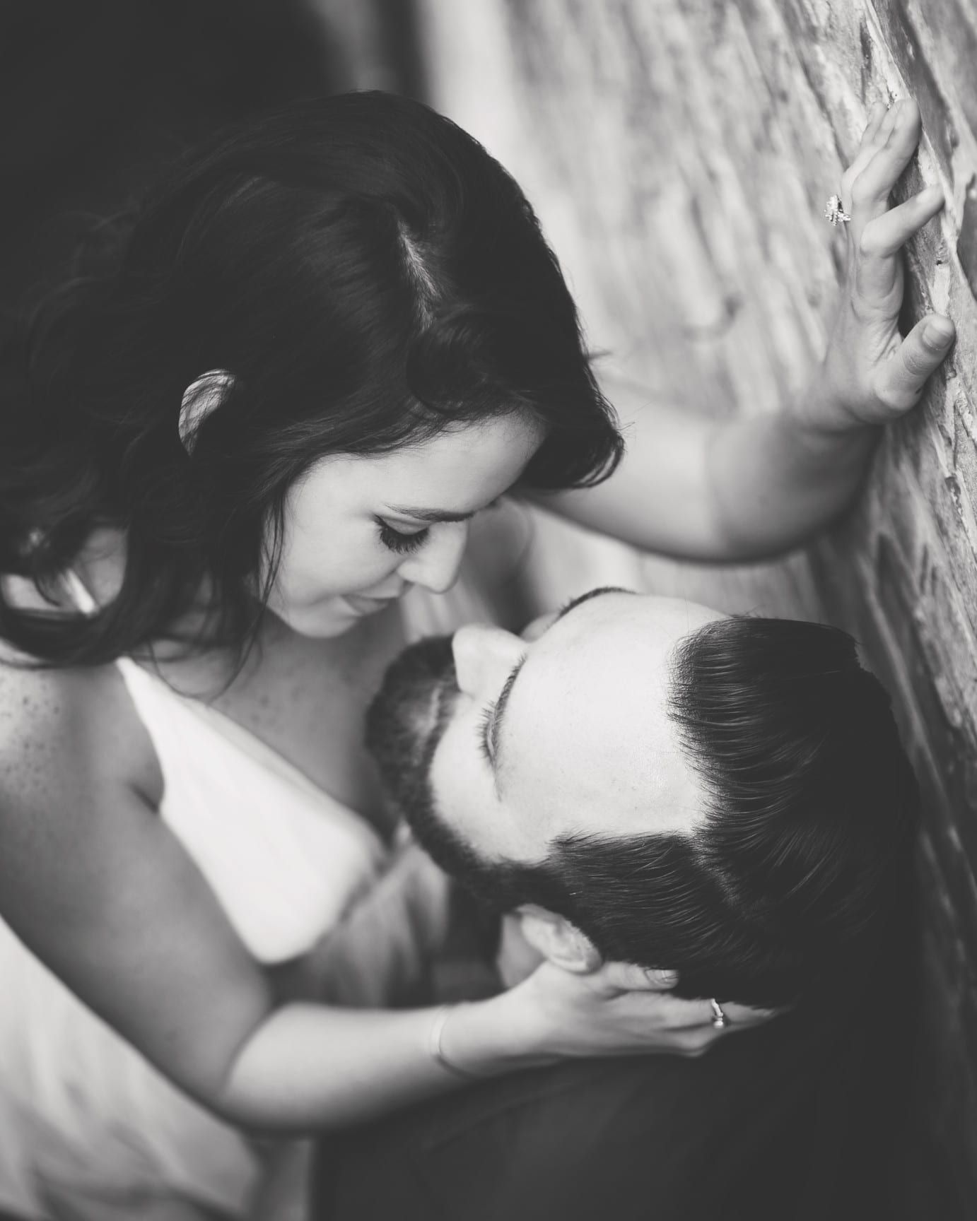 Woman gazing at man; both close, near brick wall. Black and white photo.