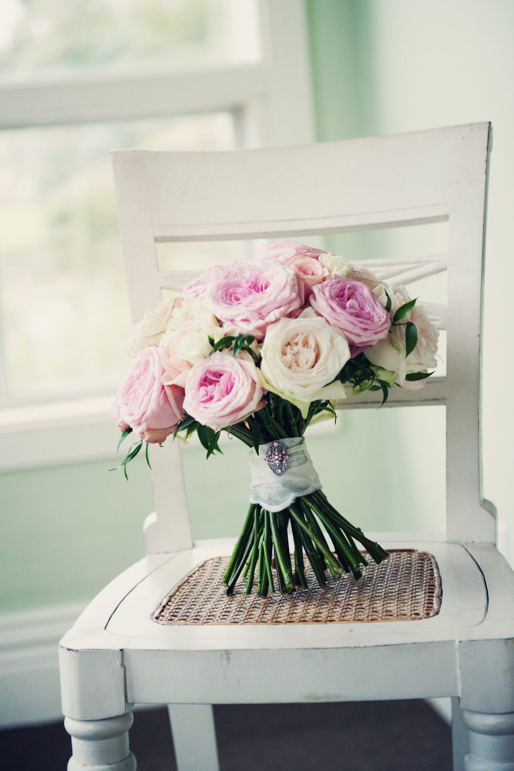 Wedding bouquet on a white chair; pink and cream roses, light green foliage.