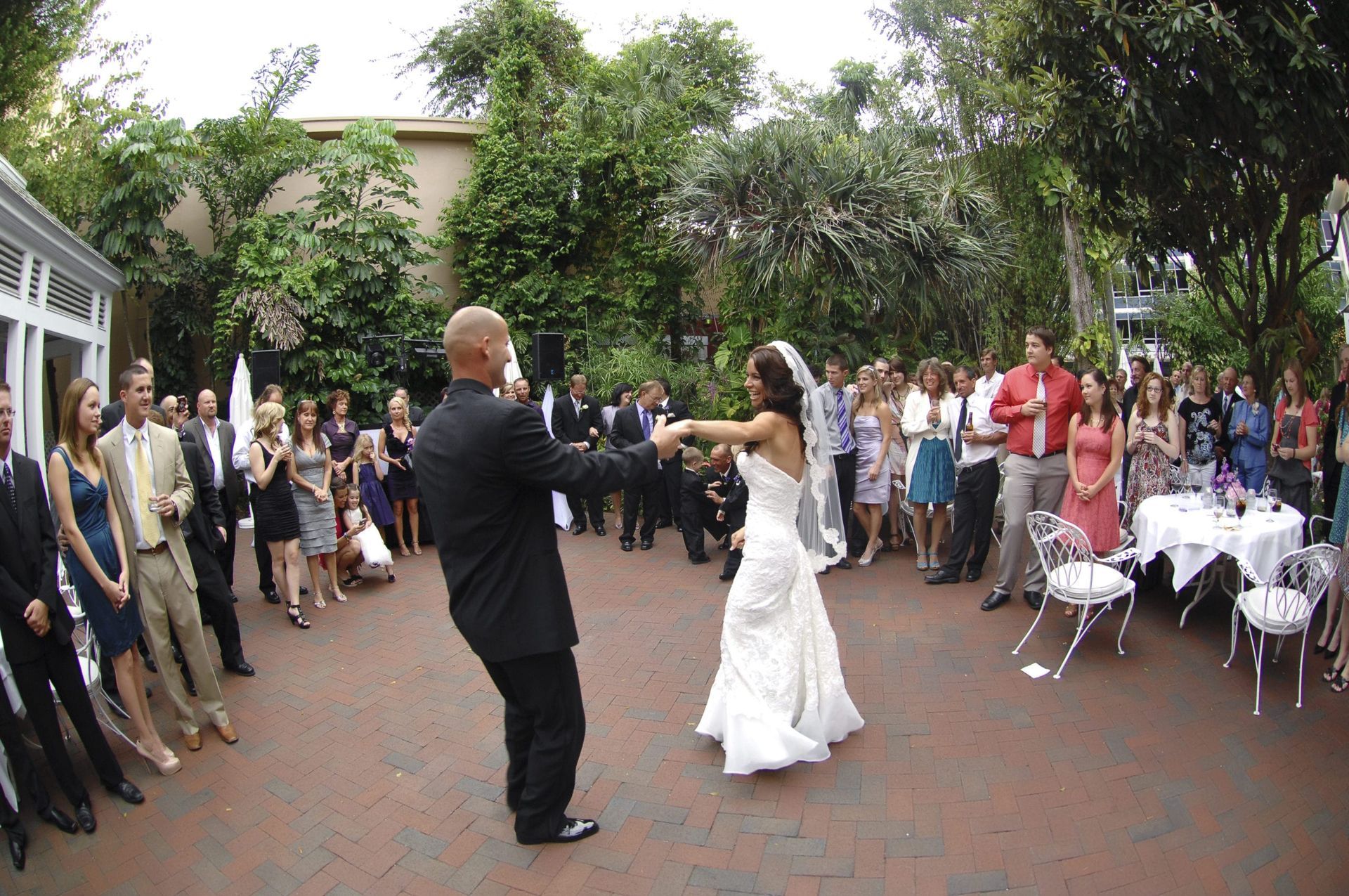 Bride and groom dancing at their wedding, surrounded by guests in a garden setting.