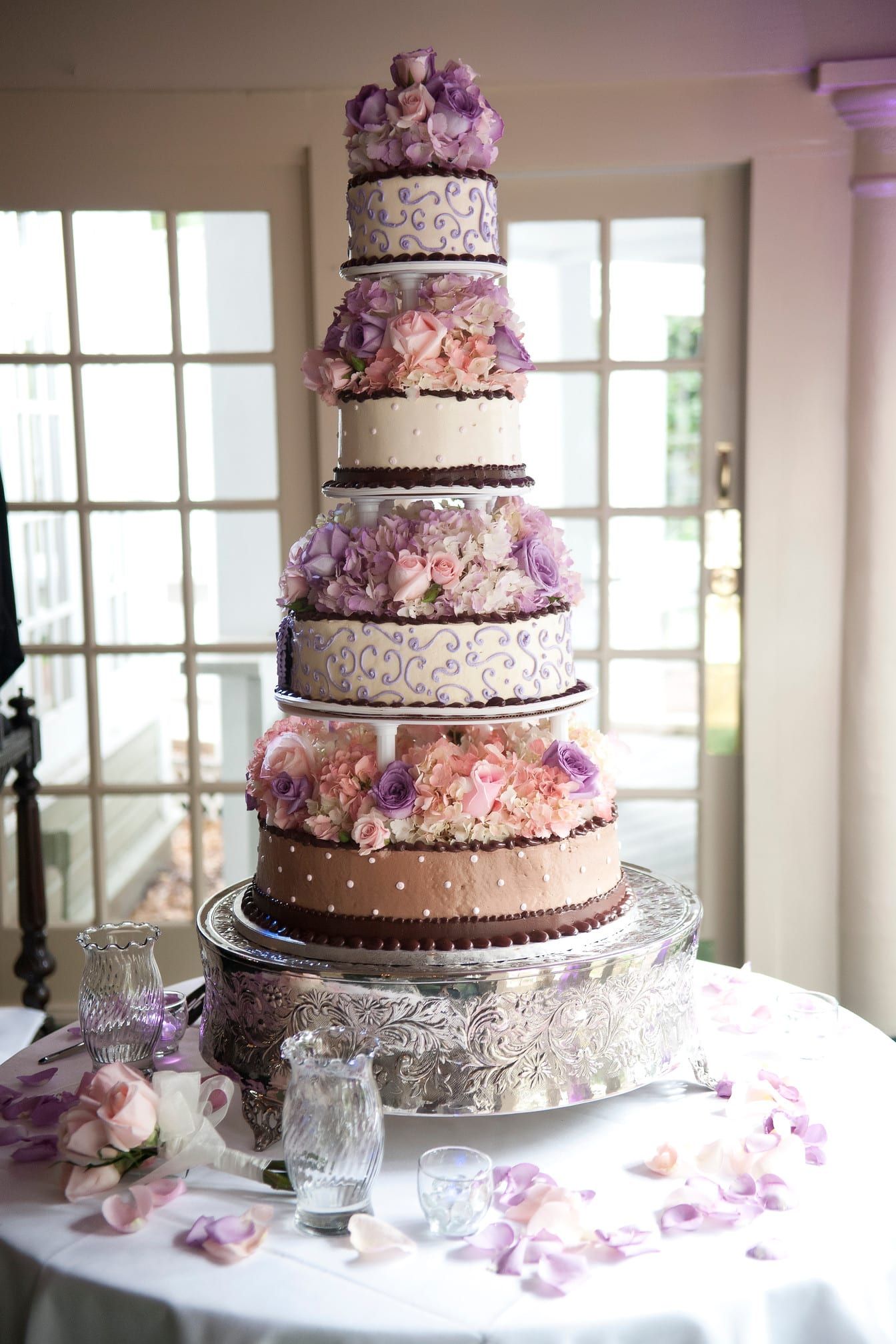 Tall, multi-tiered wedding cake, decorated with flowers, on a silver stand.